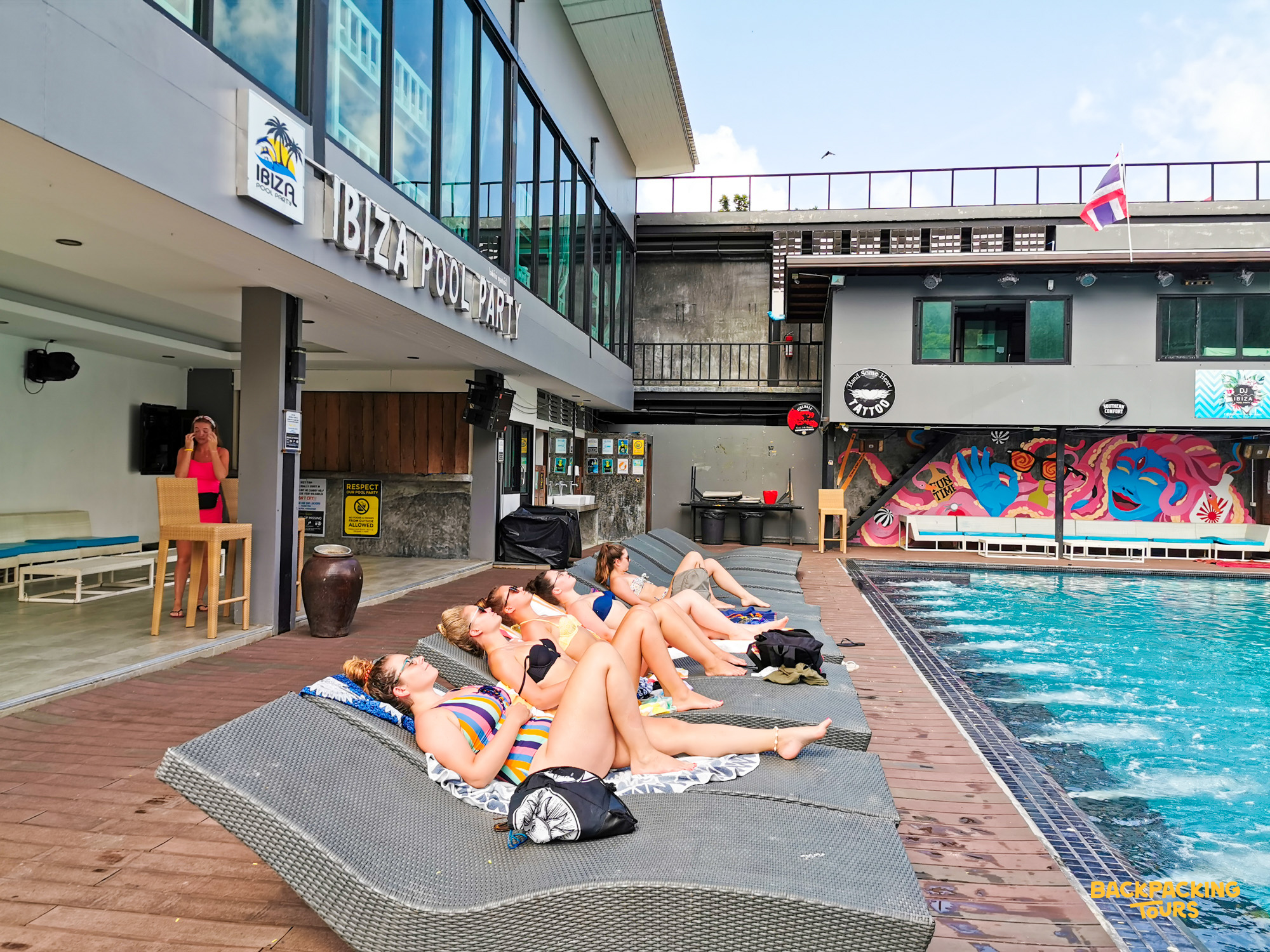 Young women sunbathing by the pool at a lively hostel in Koh Phi Phi, Thailand.
