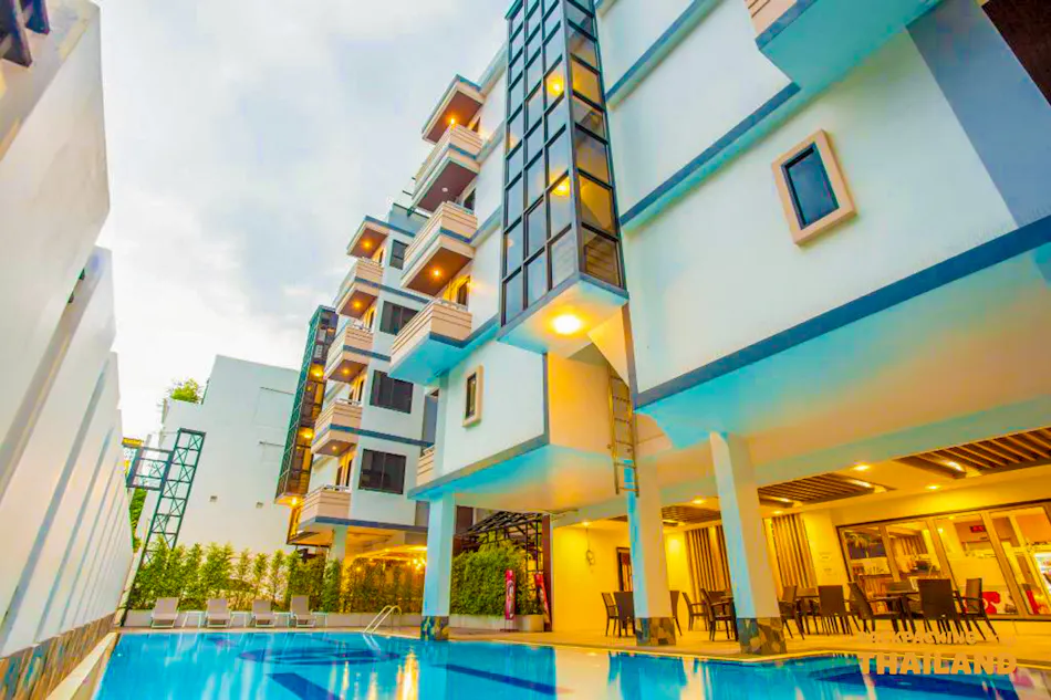A modern hotel building featuring a refreshing blue swimming pool and shaded outdoor lounge area in Bangkok.