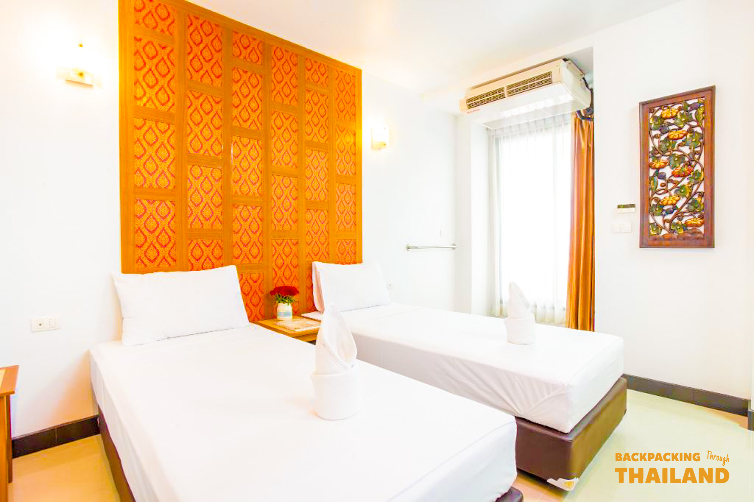 A bright and clean hotel room with two single beds and traditional Thai decor.