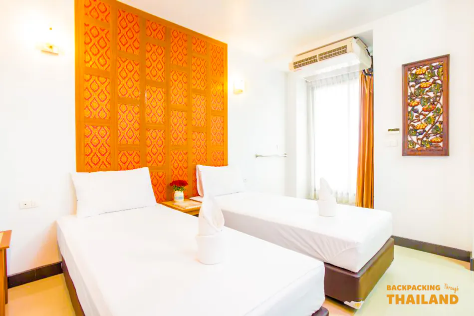 A bright and clean hotel room with two single beds and traditional Thai decor.