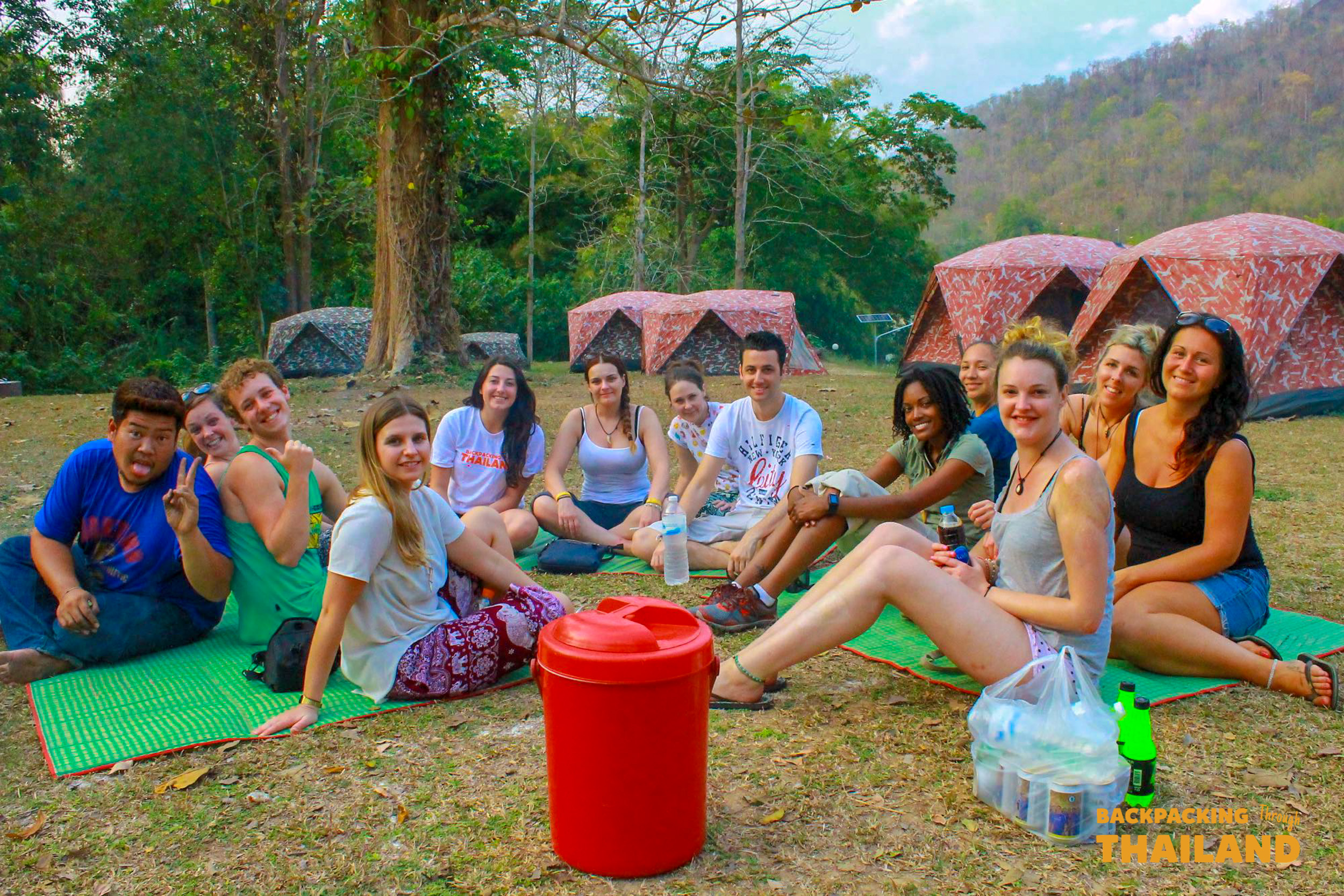 A happy group of backpackers relaxing on mats at a campsite in Erawan National Park.
