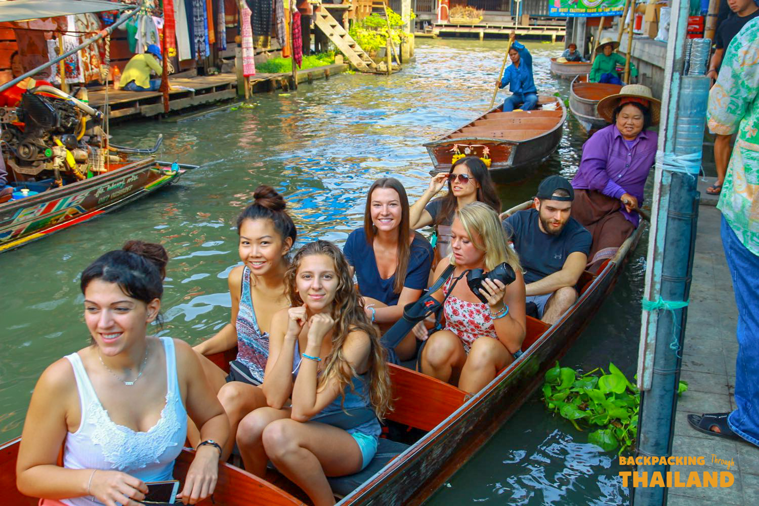 Backpackers riding paddle boat through Damnoen Saduak canals.