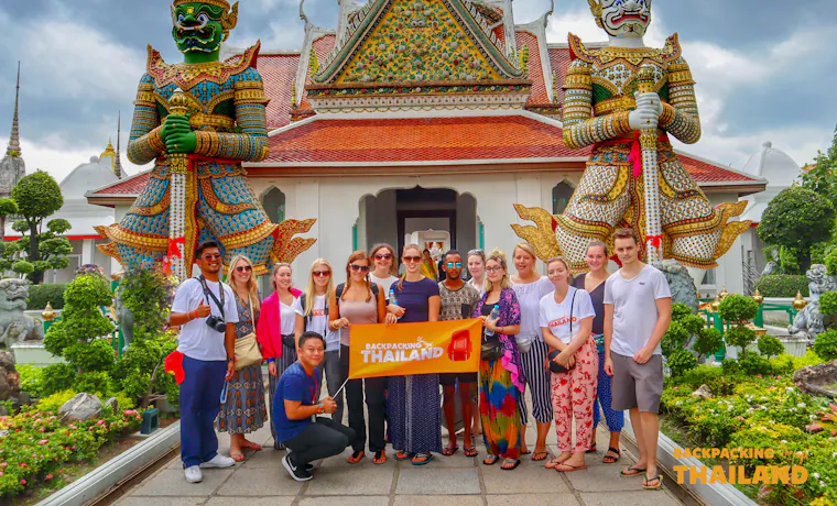 Happy backpackers pose with their tour banner before the giant guardian statues at Wat Arun, Bangkok.