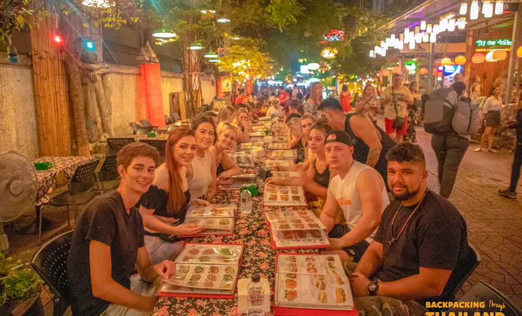 Young travelers share a fun group dinner at a bustling outdoor restaurant in Bangkok.