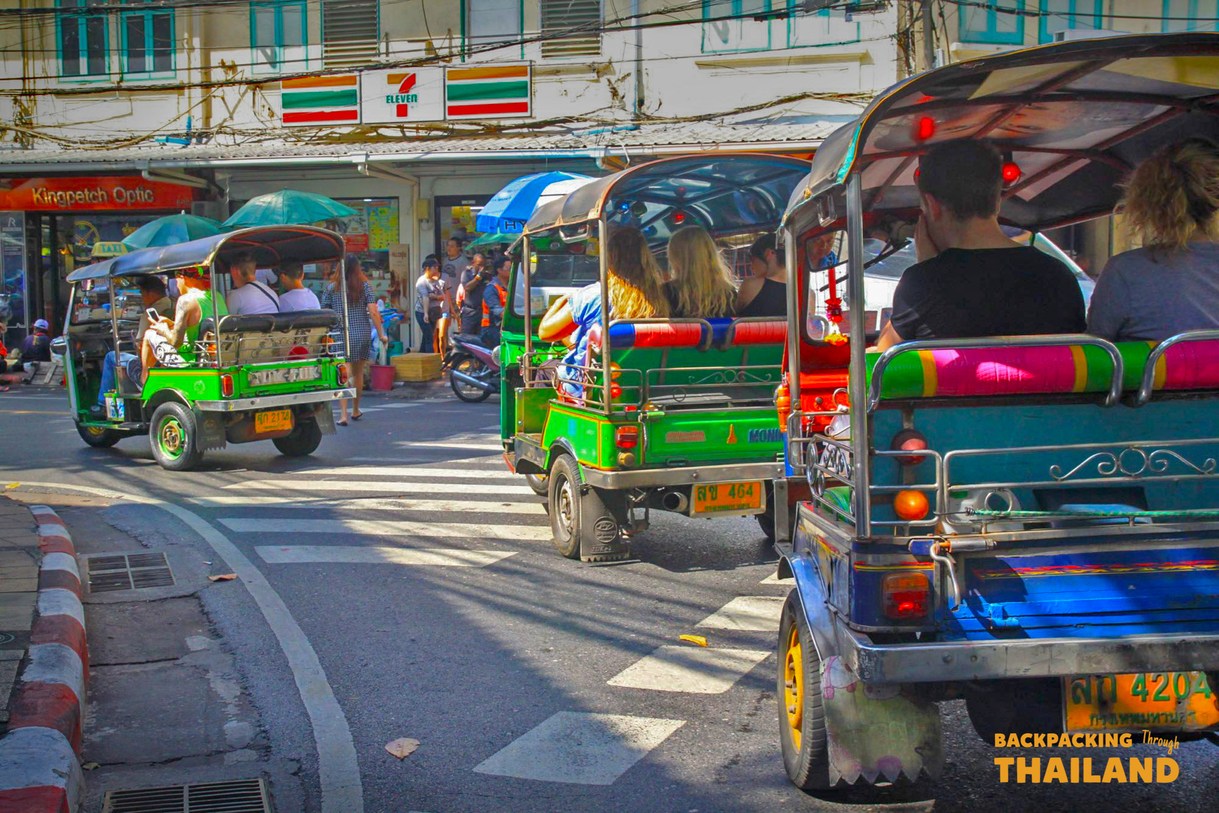 Colorful tuk-tuks with passengers navigate a busy street in Bangkok, Thailand.