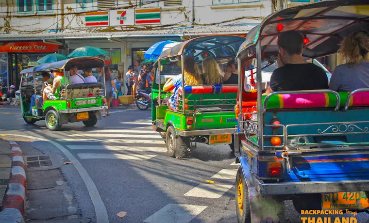 Colorful tuk-tuks with passengers navigate a busy street in Bangkok, Thailand.