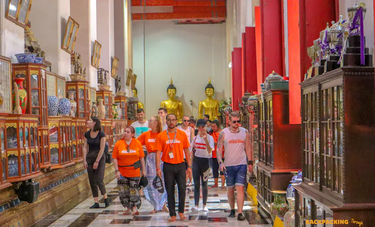 Tourists exploring a richly decorated Thai temple in Singburi with golden Buddha statues.