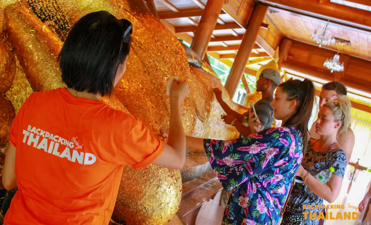 Backpackers reverently apply gold leaf to a large golden Buddha statue inside a temple in Singburi.