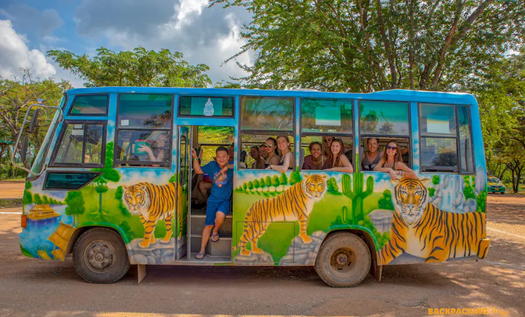 Happy backpackers enjoy a ride on a colorful tiger-painted bus at Erawan National Park in Thailand.