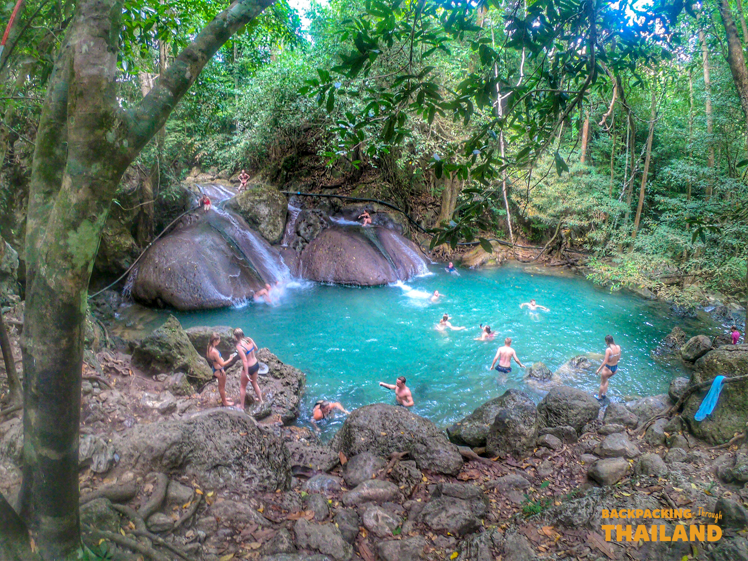 People swim and relax in the refreshing emerald pools of Erawan National Park waterfalls, Thailand.
