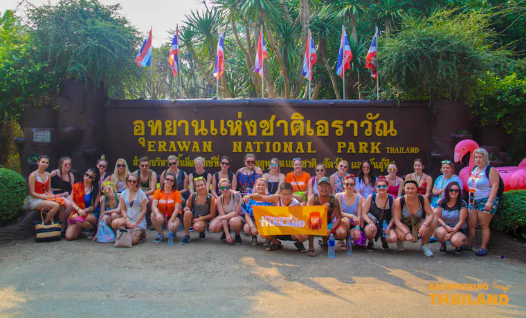 Happy backpackers gather at the Erawan National Park entrance, ready to explore the waterfalls and jungle.