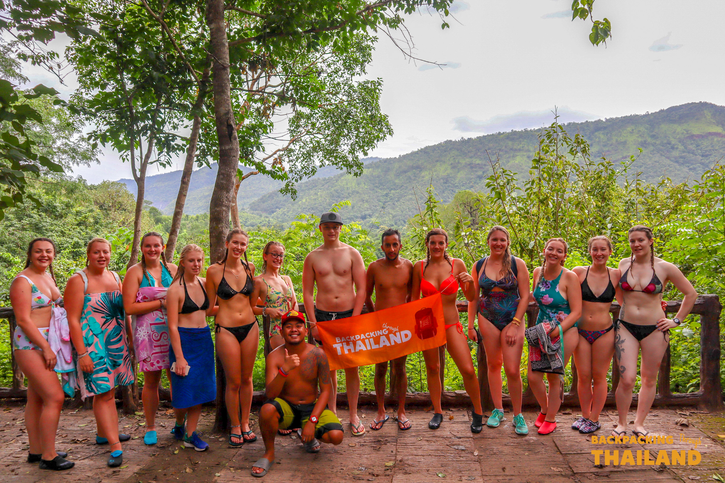 Smiling backpackers in swimwear gather for a group photo amidst the lush jungle of Erawan National Park.