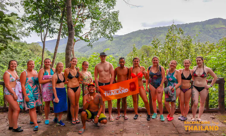 Smiling backpackers in swimwear gather for a group photo amidst the lush jungle of Erawan National Park.