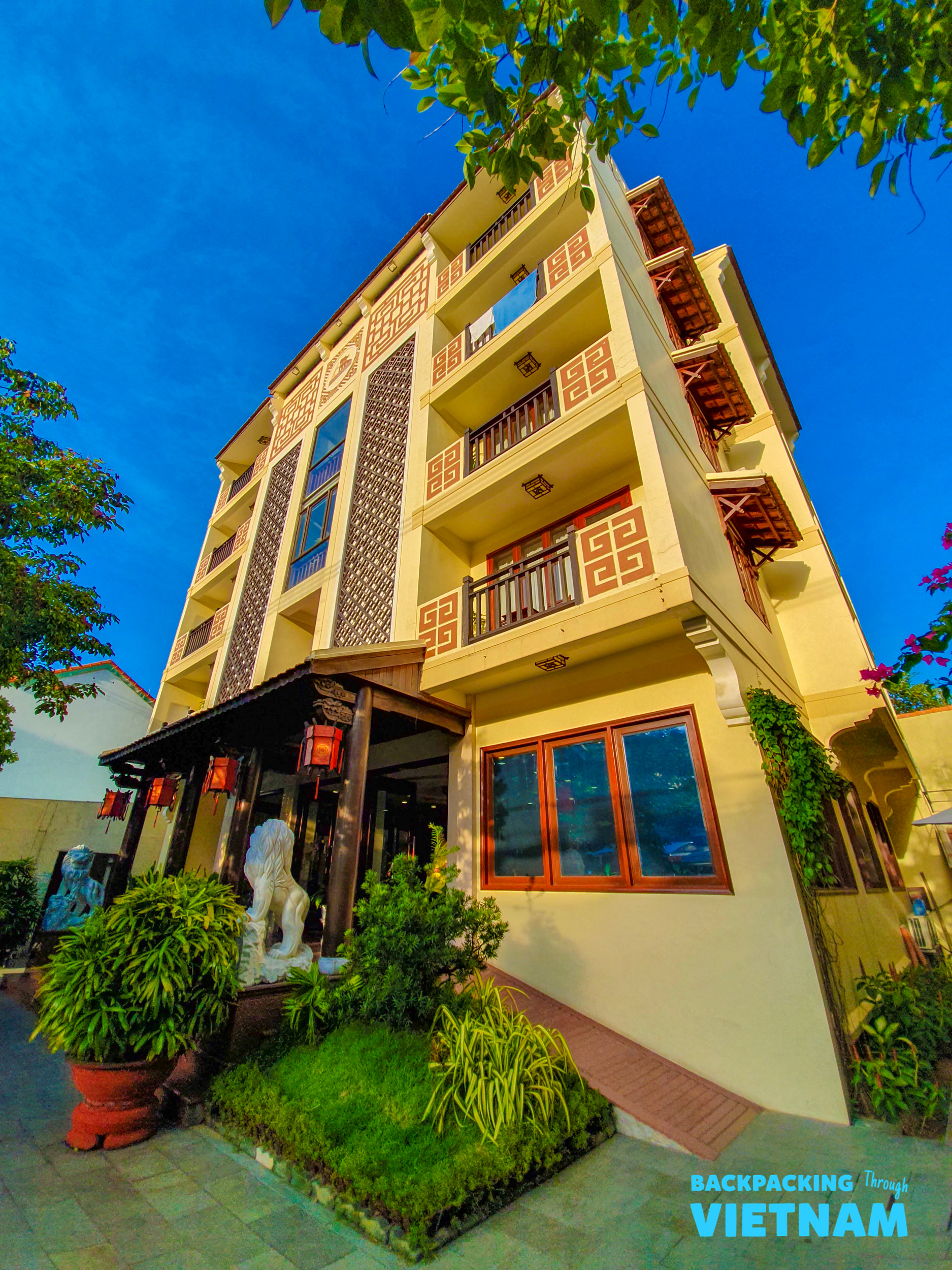A charming multi-story hotel with traditional Vietnamese architecture, decorative balconies, and red lanterns at the entrance in Hoi An.