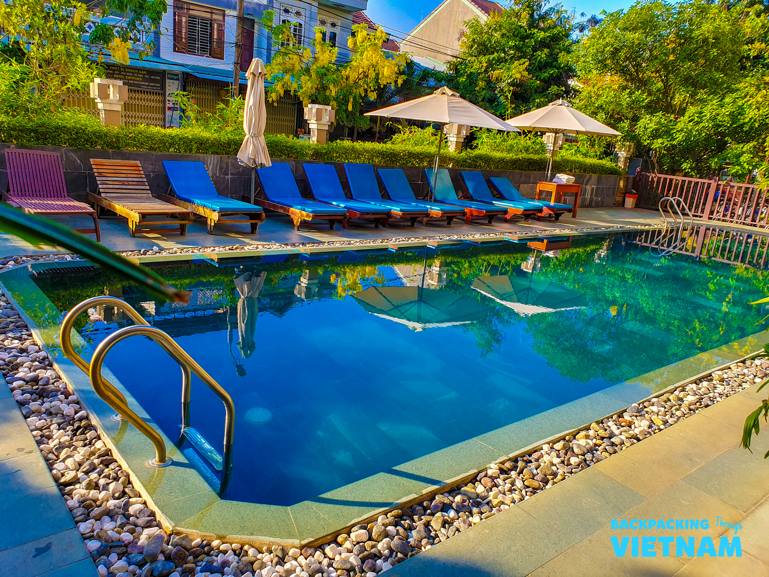 Inviting blue swimming pool with sun loungers and umbrellas at a sunny Hoi An hotel.