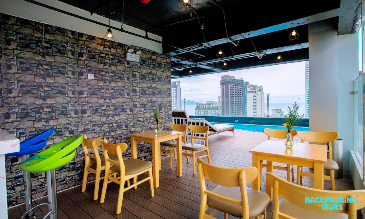 Inviting rooftop dining area with wooden tables, a pool, and city views in Nha Trang.