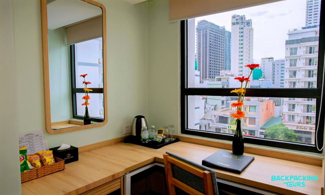 A comfortable hotel room in Nha Trang featuring a desk, fresh flowers, and a vibrant city view.