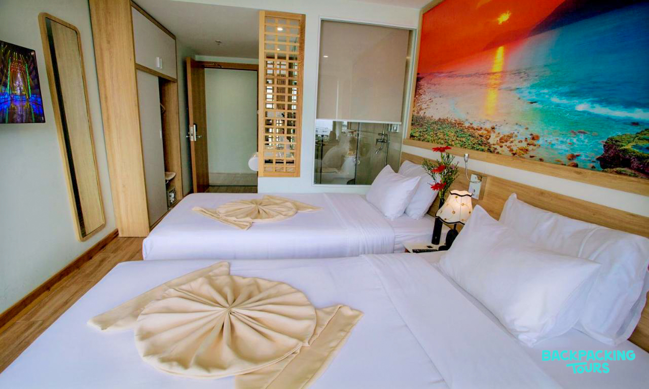 A bright and inviting hotel room in Nha Trang with two comfortable beds and a colorful abstract mural.