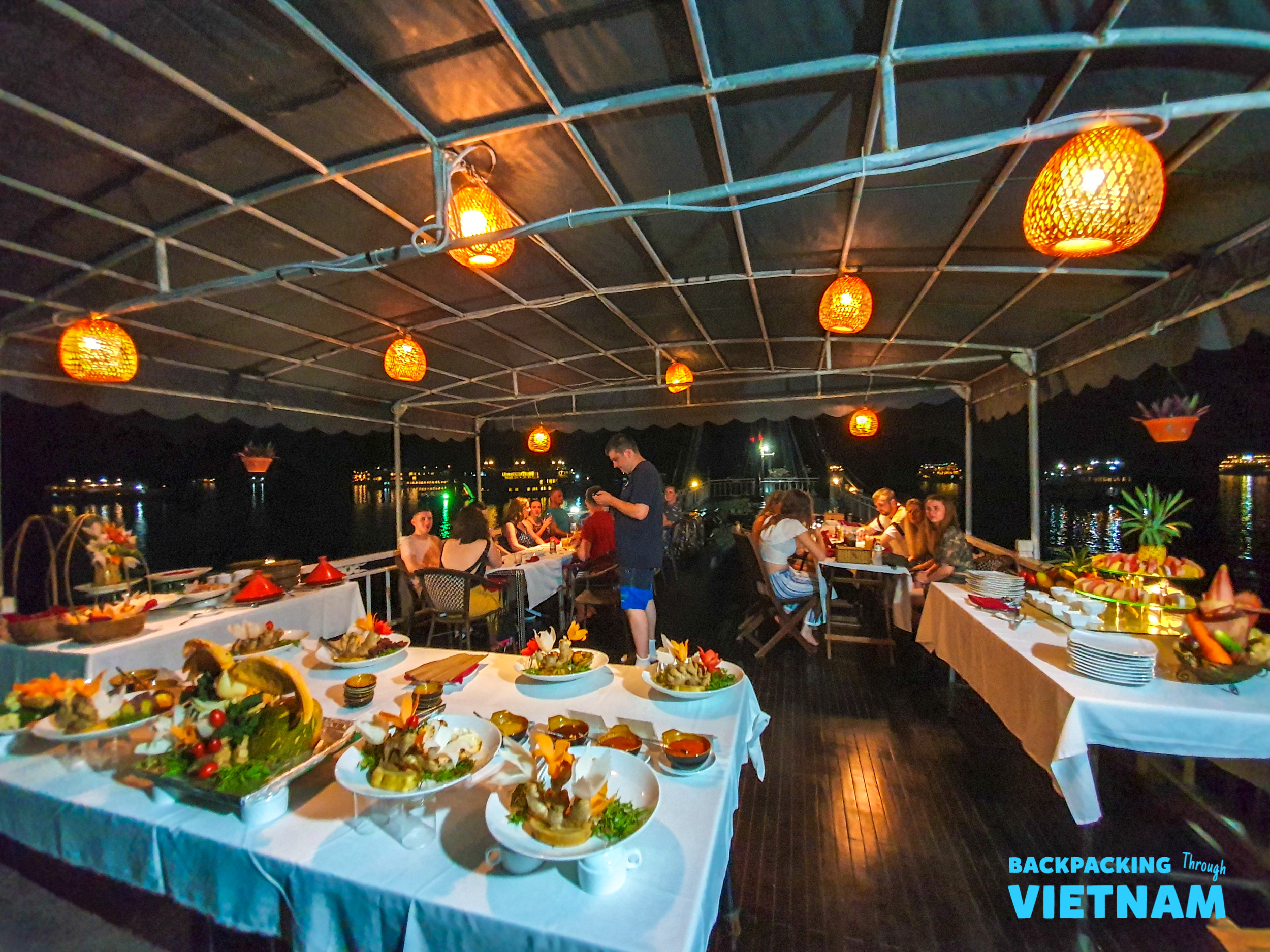 Enjoying a festive buffet dinner with fellow travelers under glowing lanterns on a Halong Bay boat.