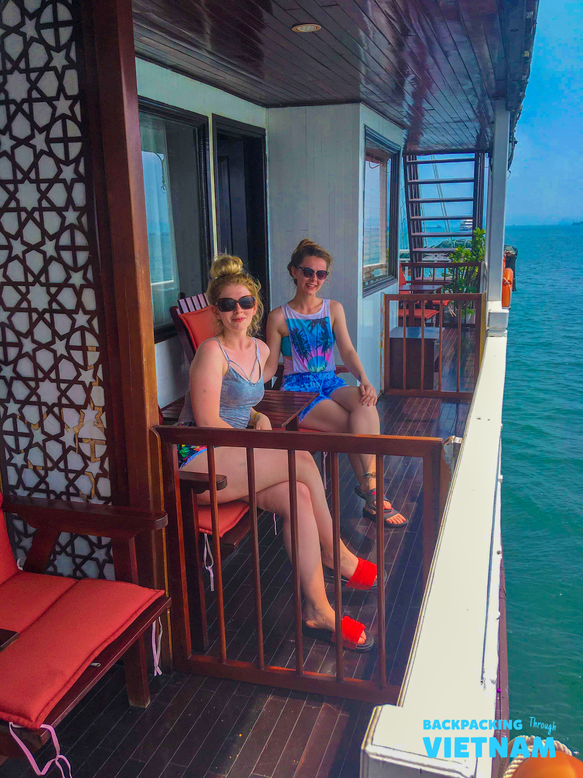 Two happy travelers enjoying the sunshine and ocean views from their Halong Bay cruise balcony.