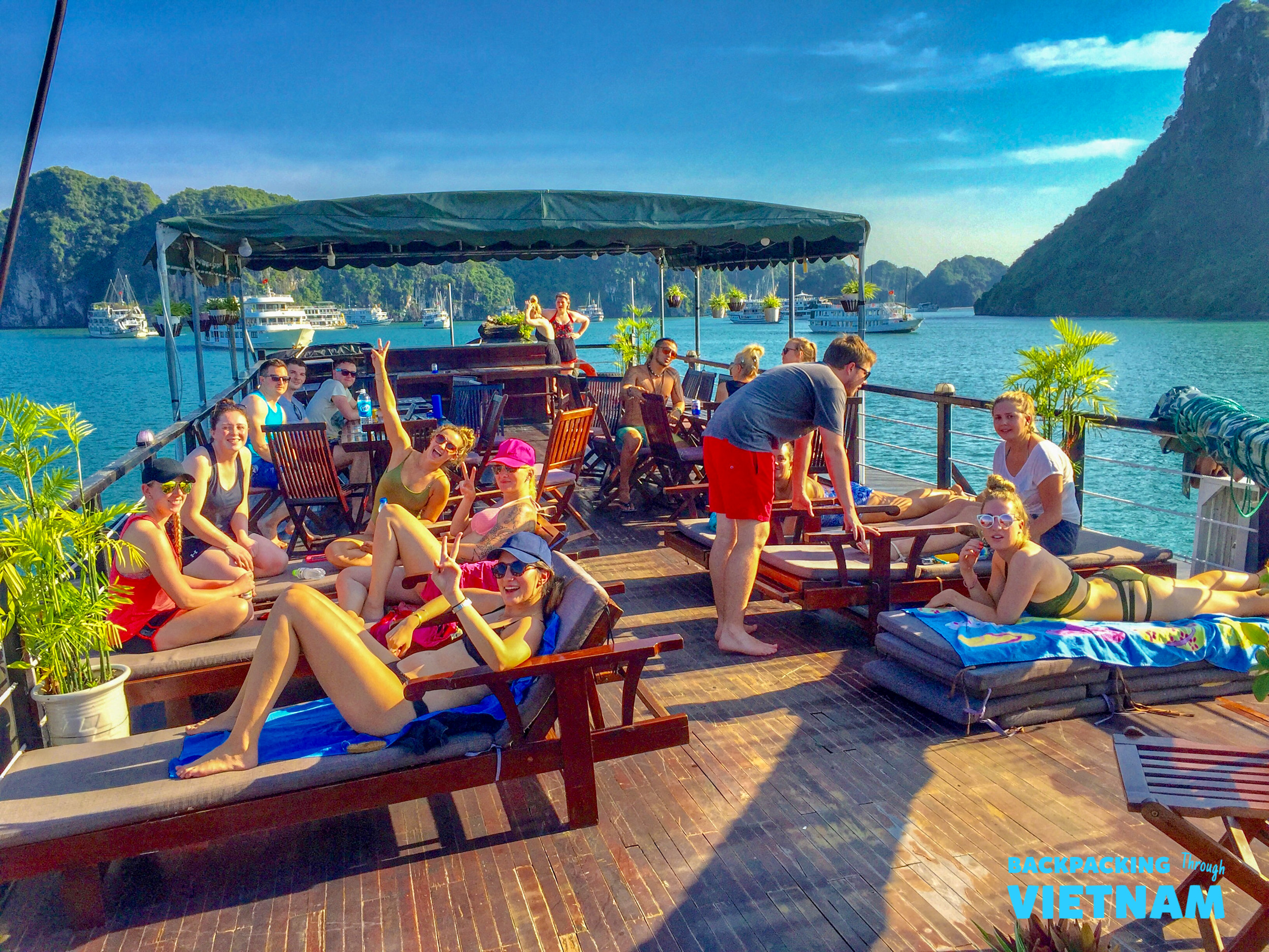 Happy backpackers relax on a boat deck, sunbathing and socializing in beautiful Halong Bay, Vietnam.