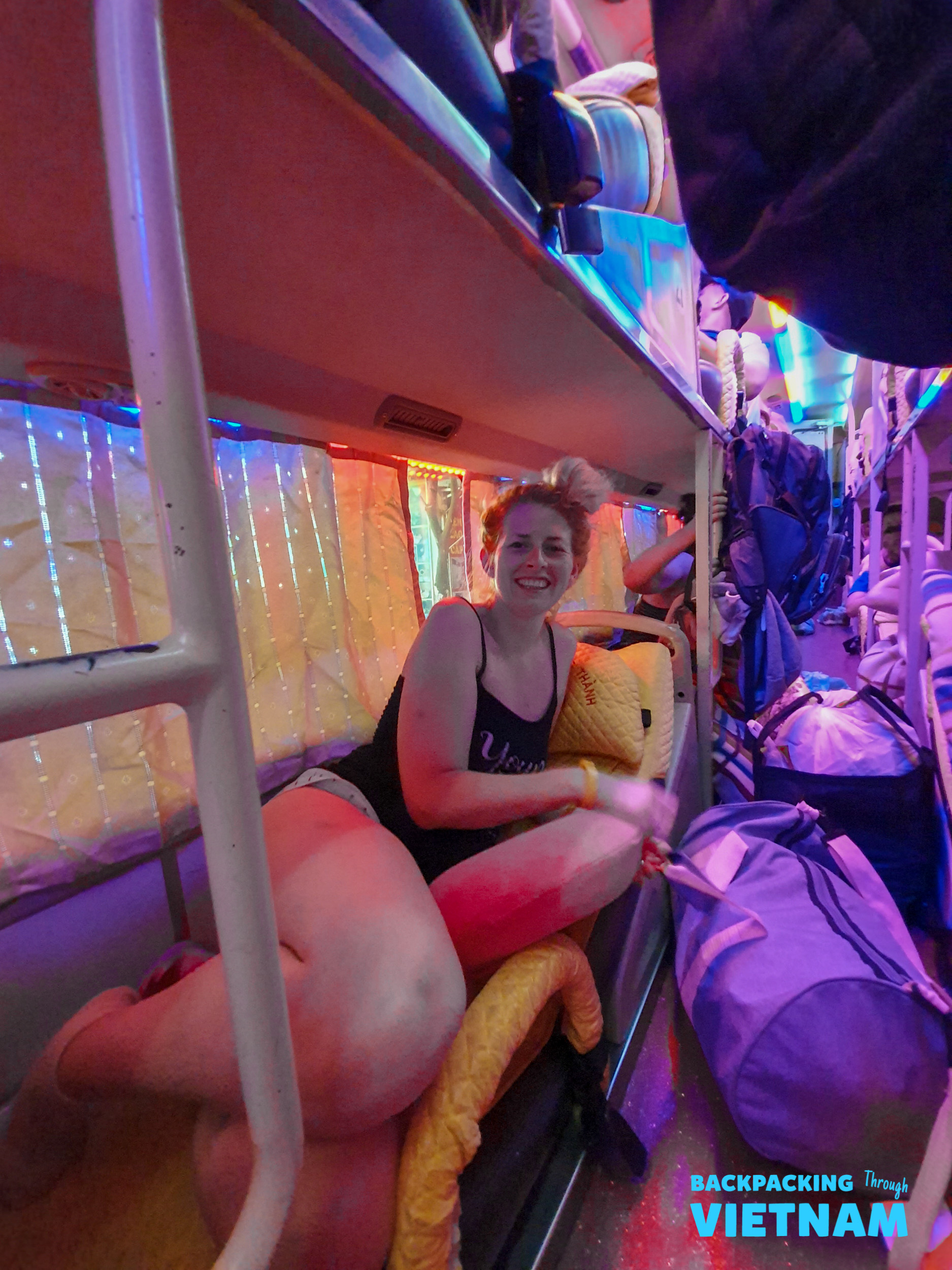A smiling backpacker relaxes in a vibrant, colorful sleeper bus bunk in Vietnam.