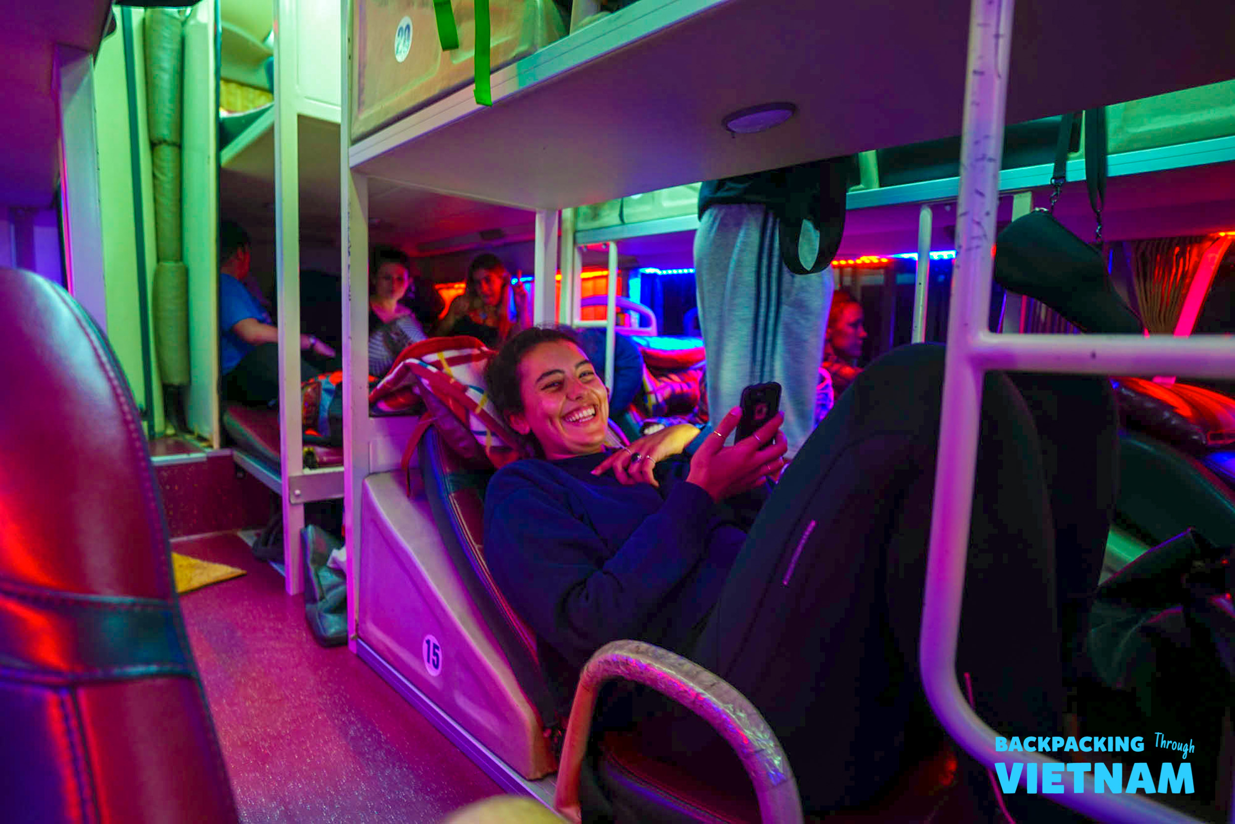 A smiling backpacker relaxes in a colorful bunk on a sleeper bus in Vietnam.