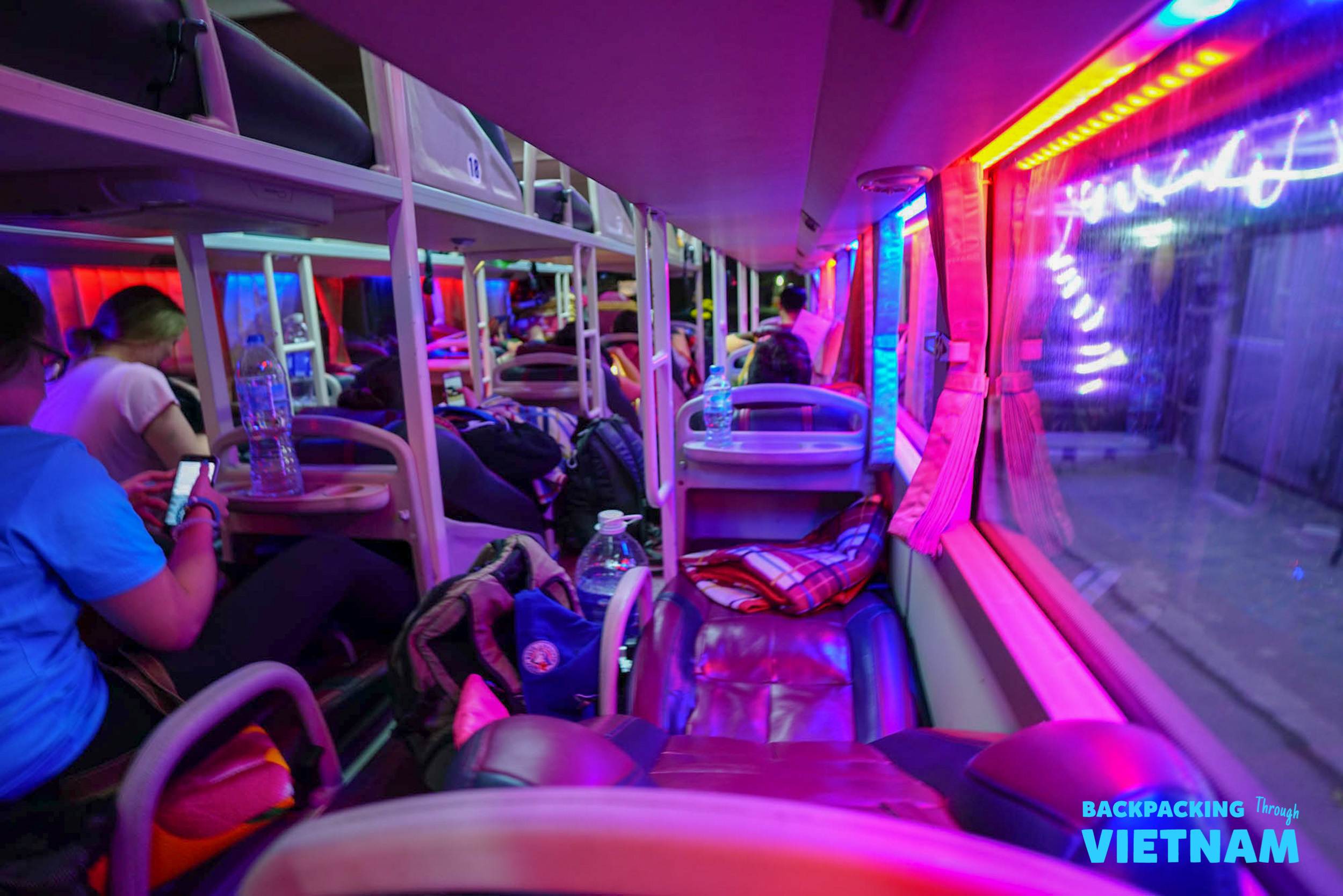 Travelers relax in their bunks on a vibrant neon-lit sleeper bus during a night journey in Vietnam.