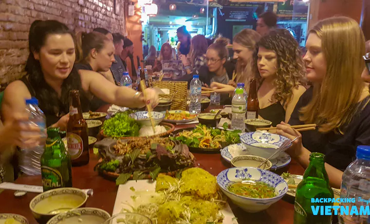 Backpackers enjoying a vibrant shared dinner with many local dishes in a lively Hanoi restaurant.