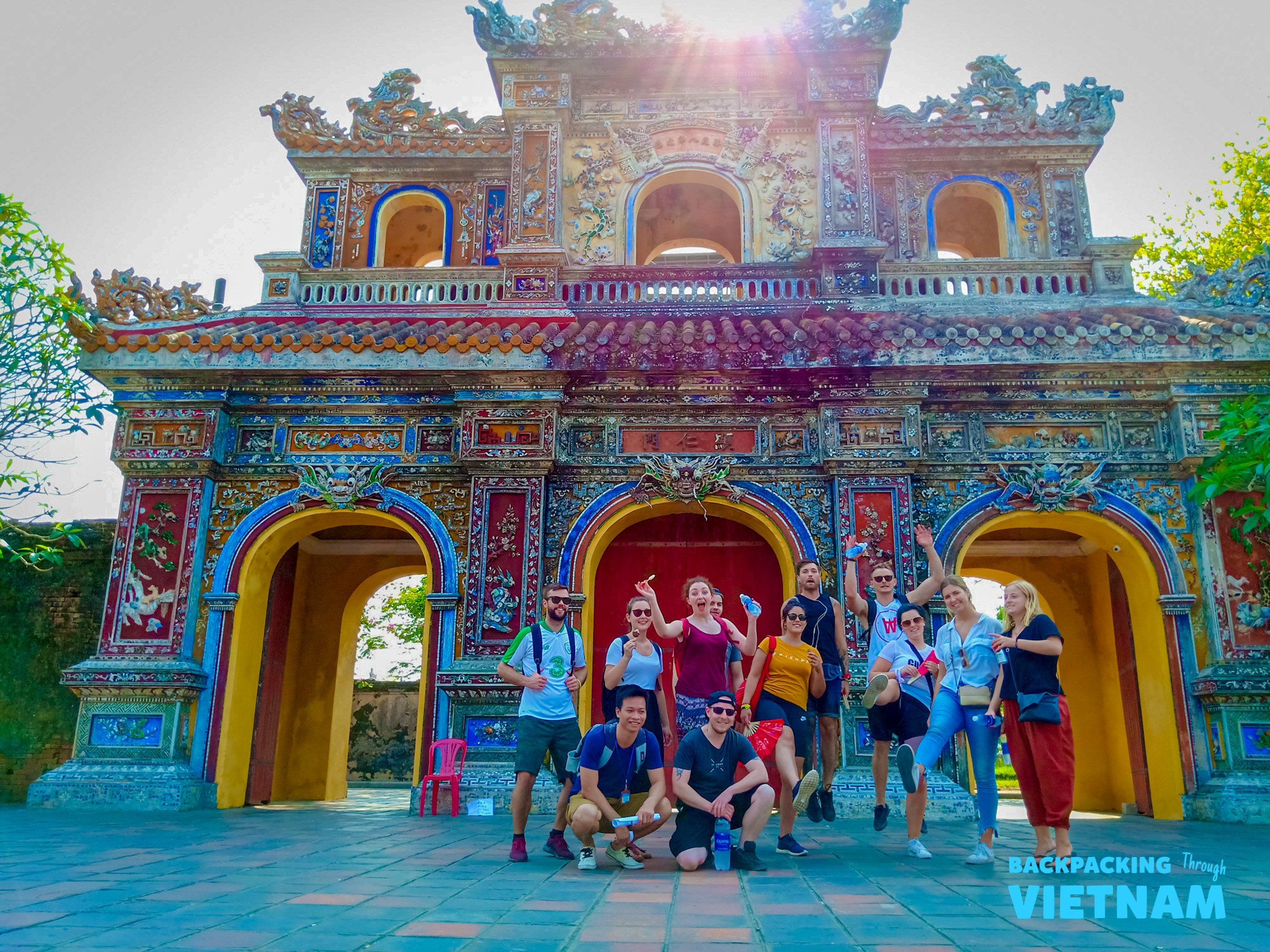 Enthusiastic backpackers pose together in front of the magnificent, colorful Imperial City gate in Hue.