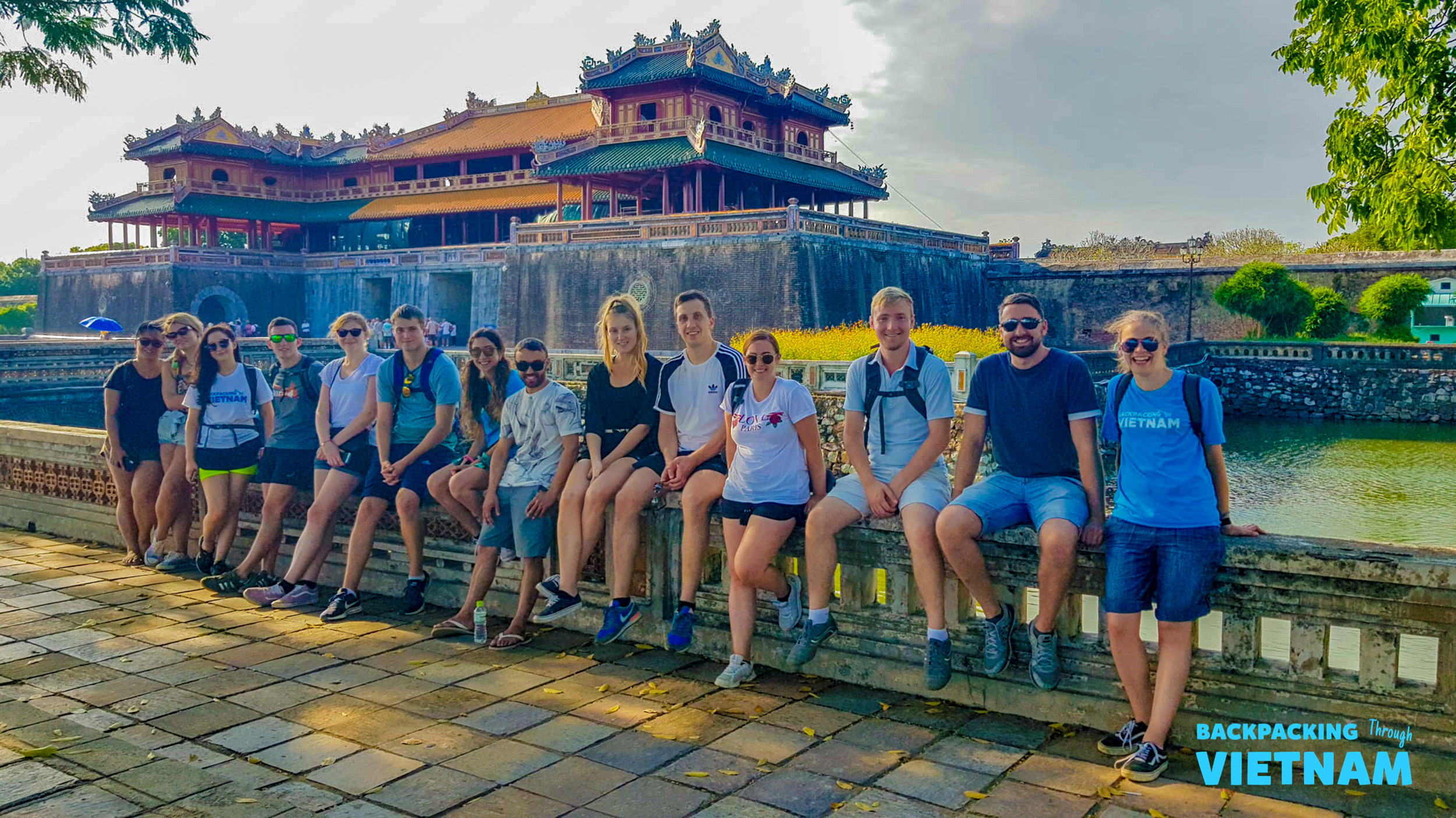 A group of happy backpackers sits on a wall overlooking the majestic Imperial City in Hue, Vietnam.