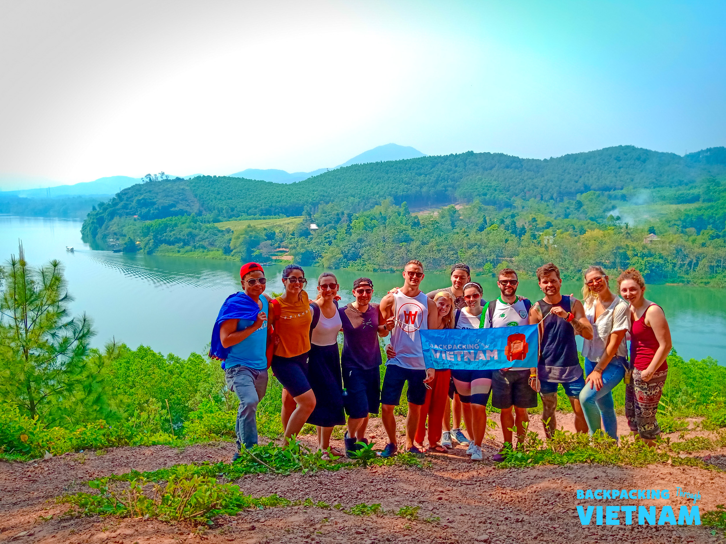 A group of happy backpackers posing on a scenic hill overlooking a tranquil lake in Vietnam.