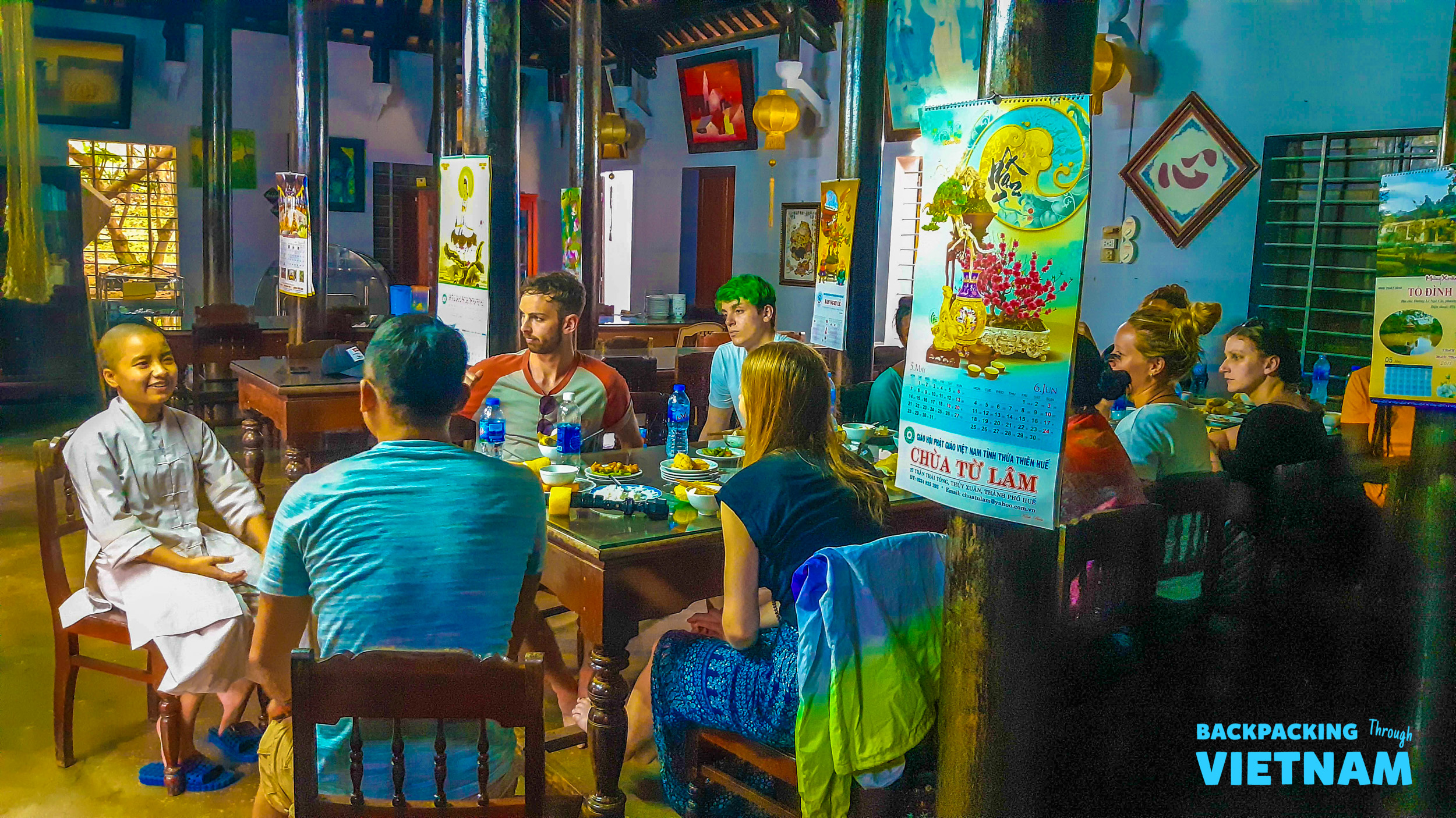 A group of backpackers and a local share a meal at a rustic restaurant in Hue, Vietnam.