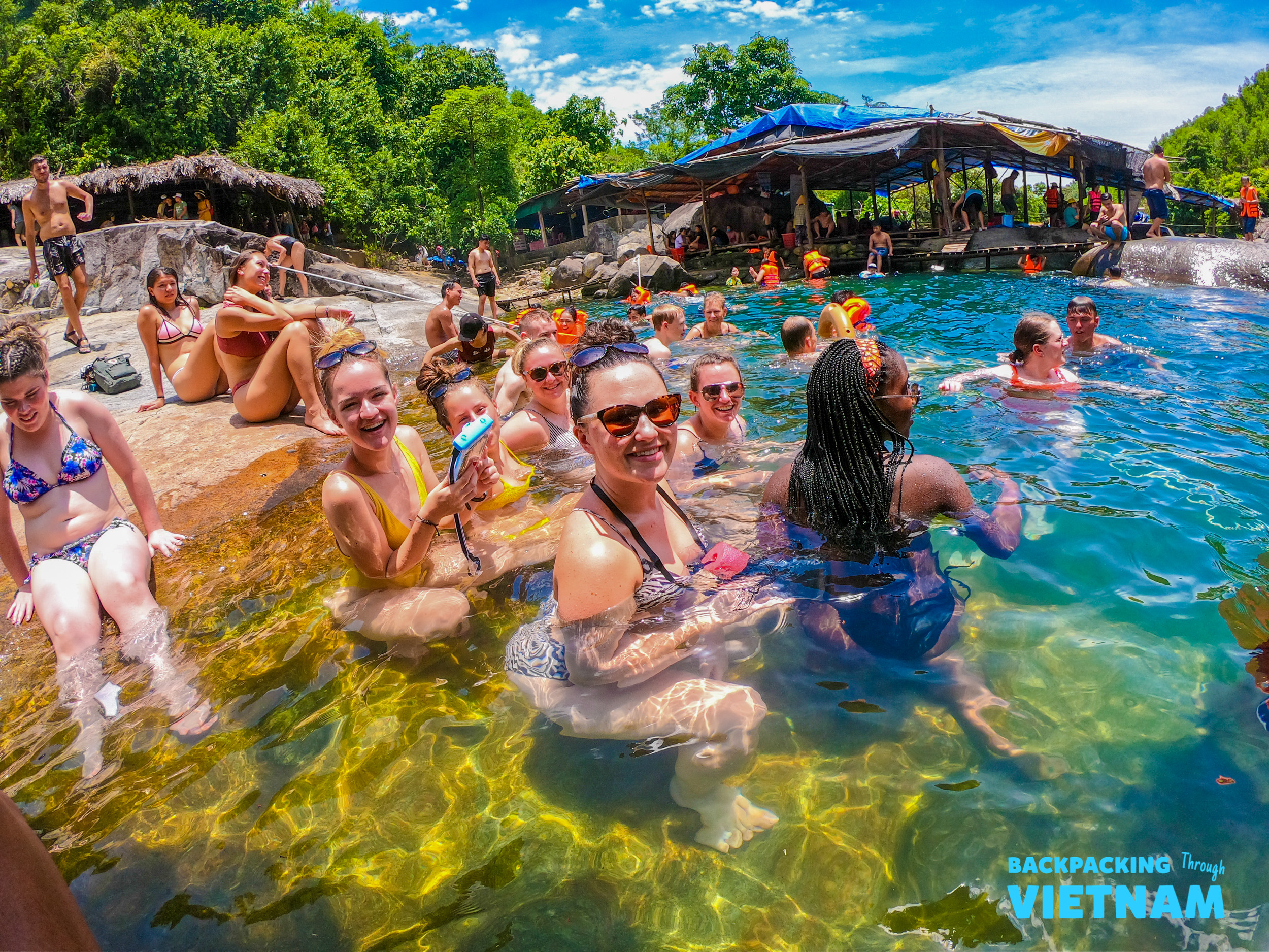 Happy backpackers cool off in a clear natural spring, surrounded by lush green trees in Vietnam.