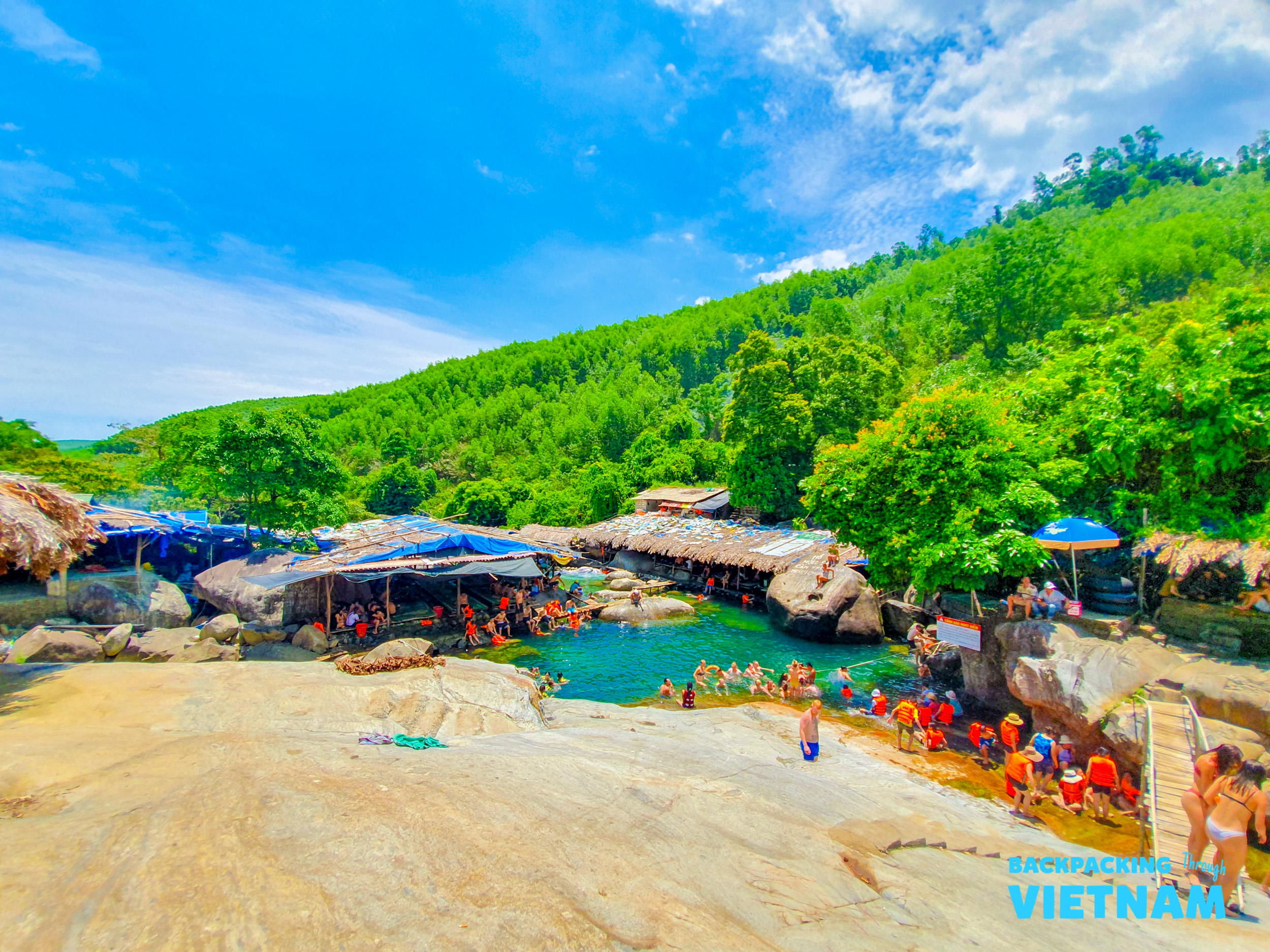 Travelers swim and relax in a beautiful natural spring surrounded by lush green hills in Vietnam.