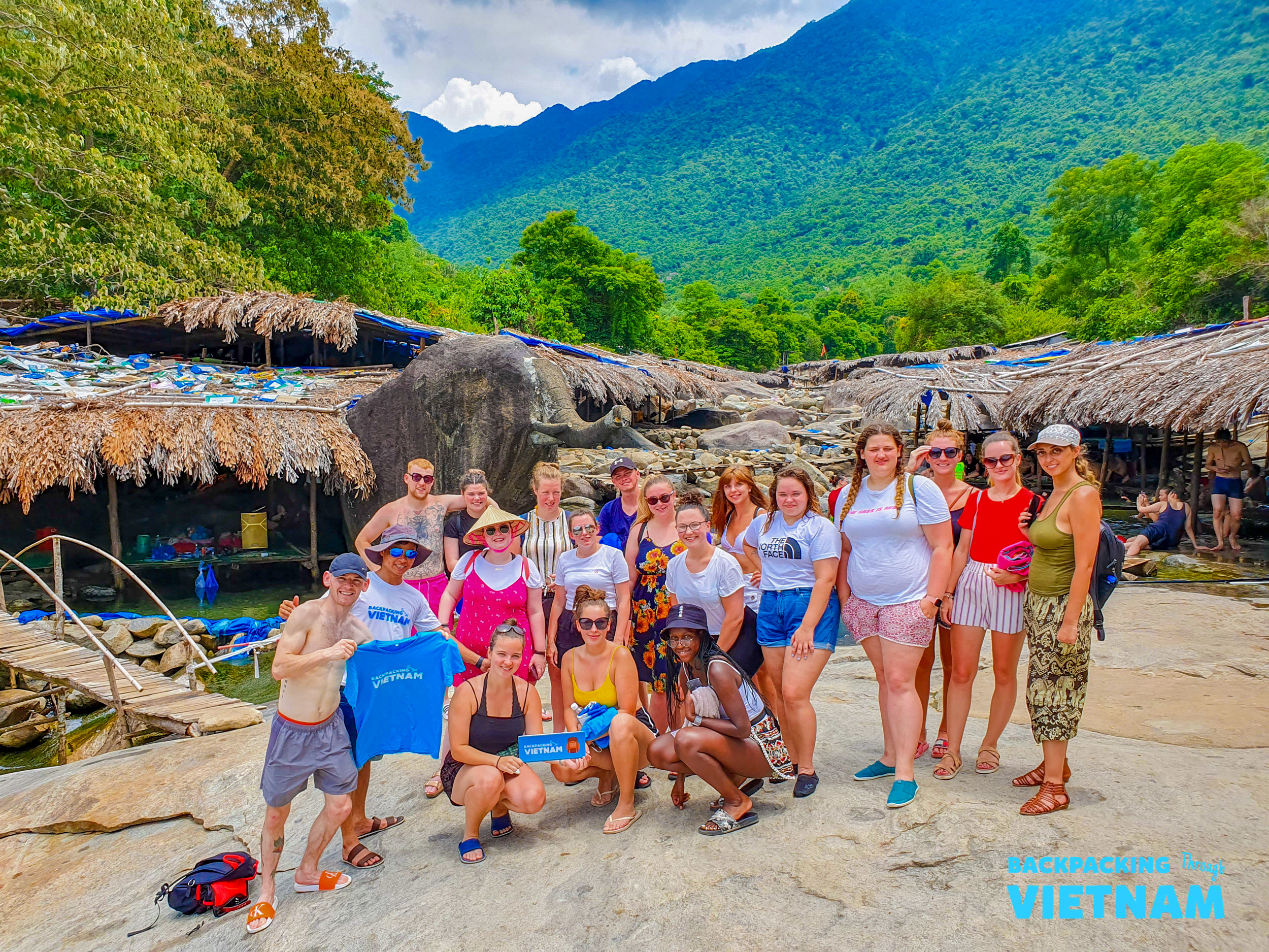 Smiling backpackers gather for a photo at a scenic natural spring in the Vietnamese mountains.