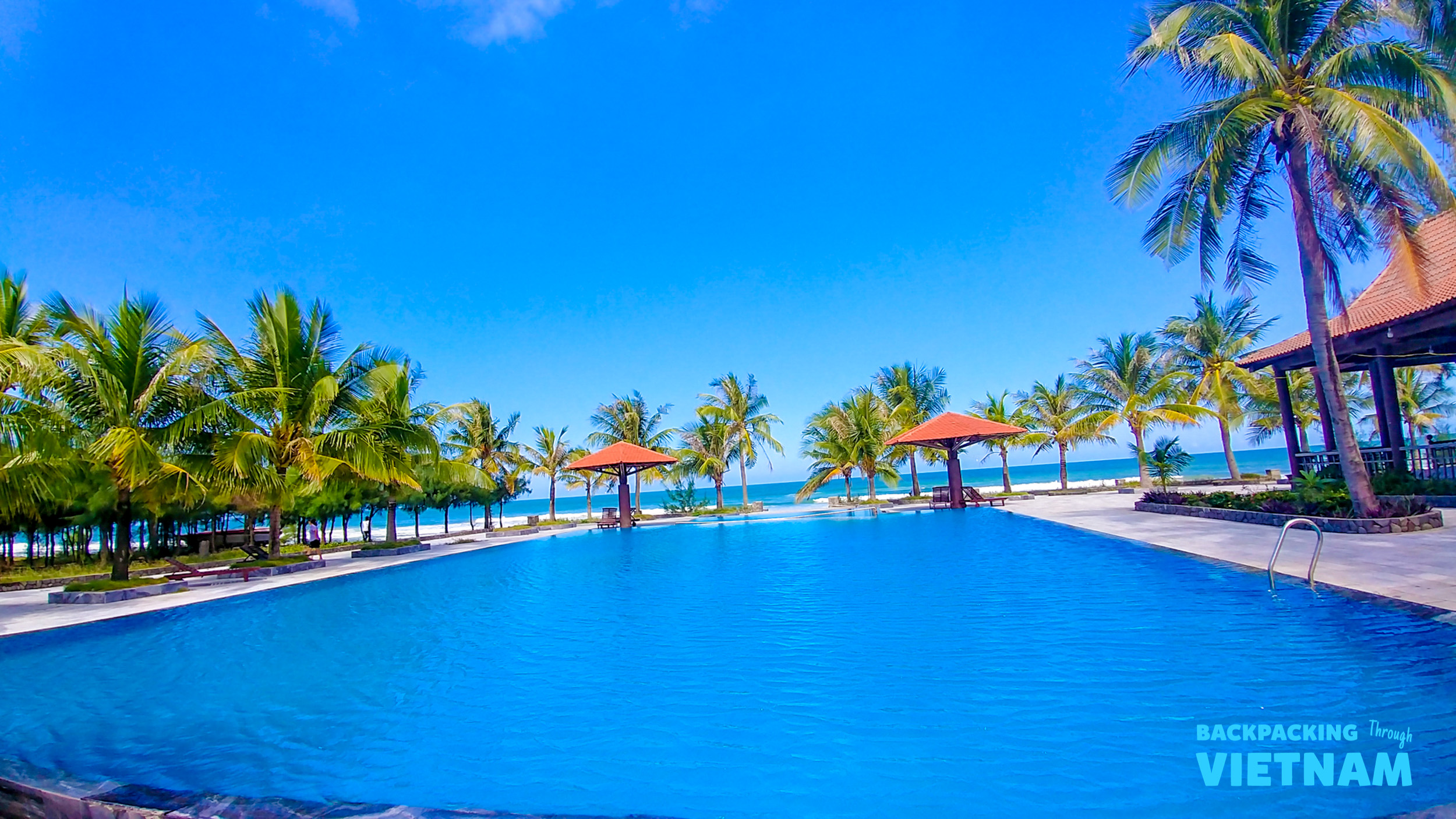 A beautiful blue swimming pool surrounded by palm trees overlooking the ocean in Hoi An, Vietnam.