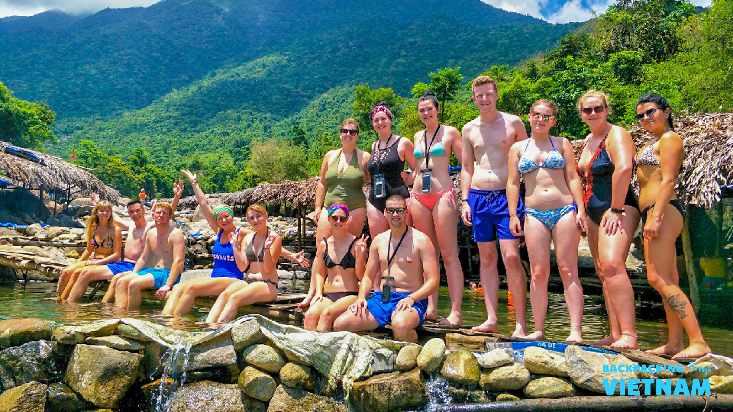 Happy backpackers relax and swim in a beautiful natural spring surrounded by lush Vietnamese mountains.