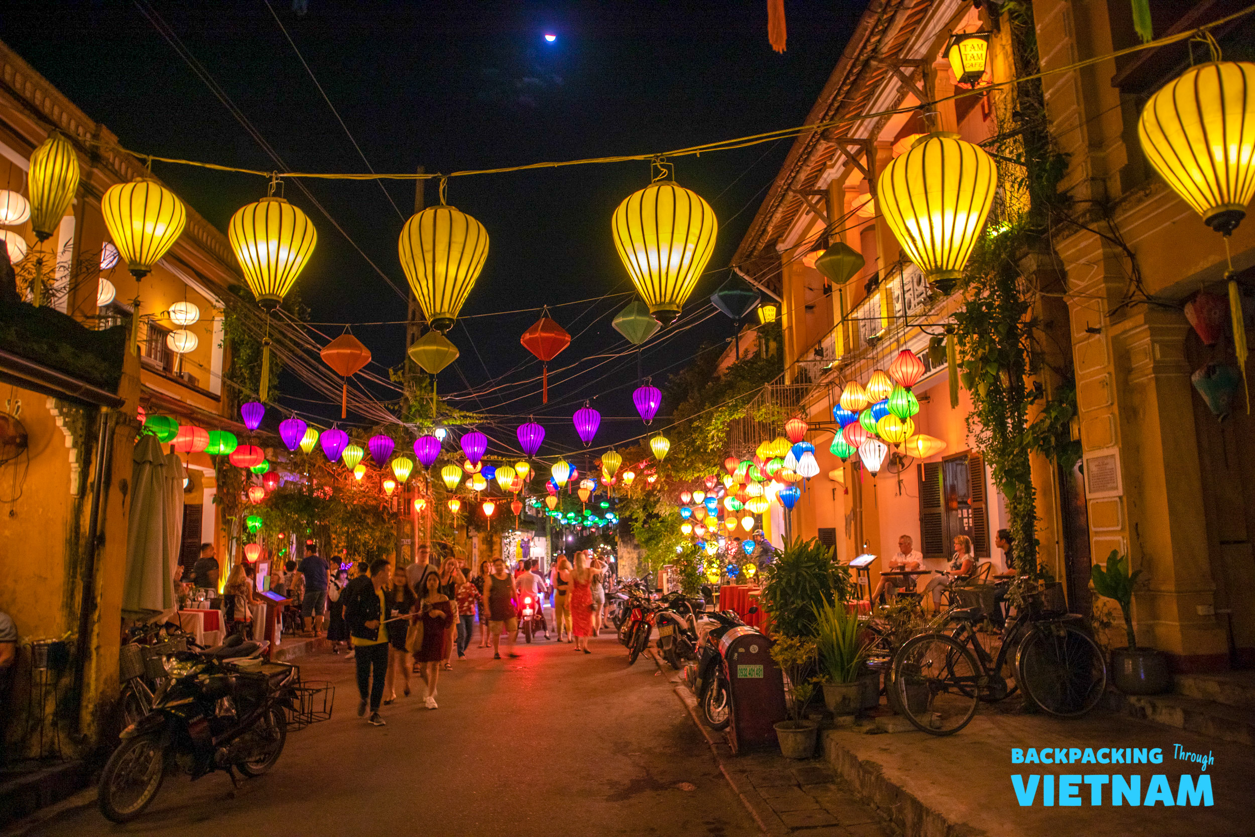 People stroll under a canopy of glowing lanterns on a vibrant night in Hoi An, Vietnam.