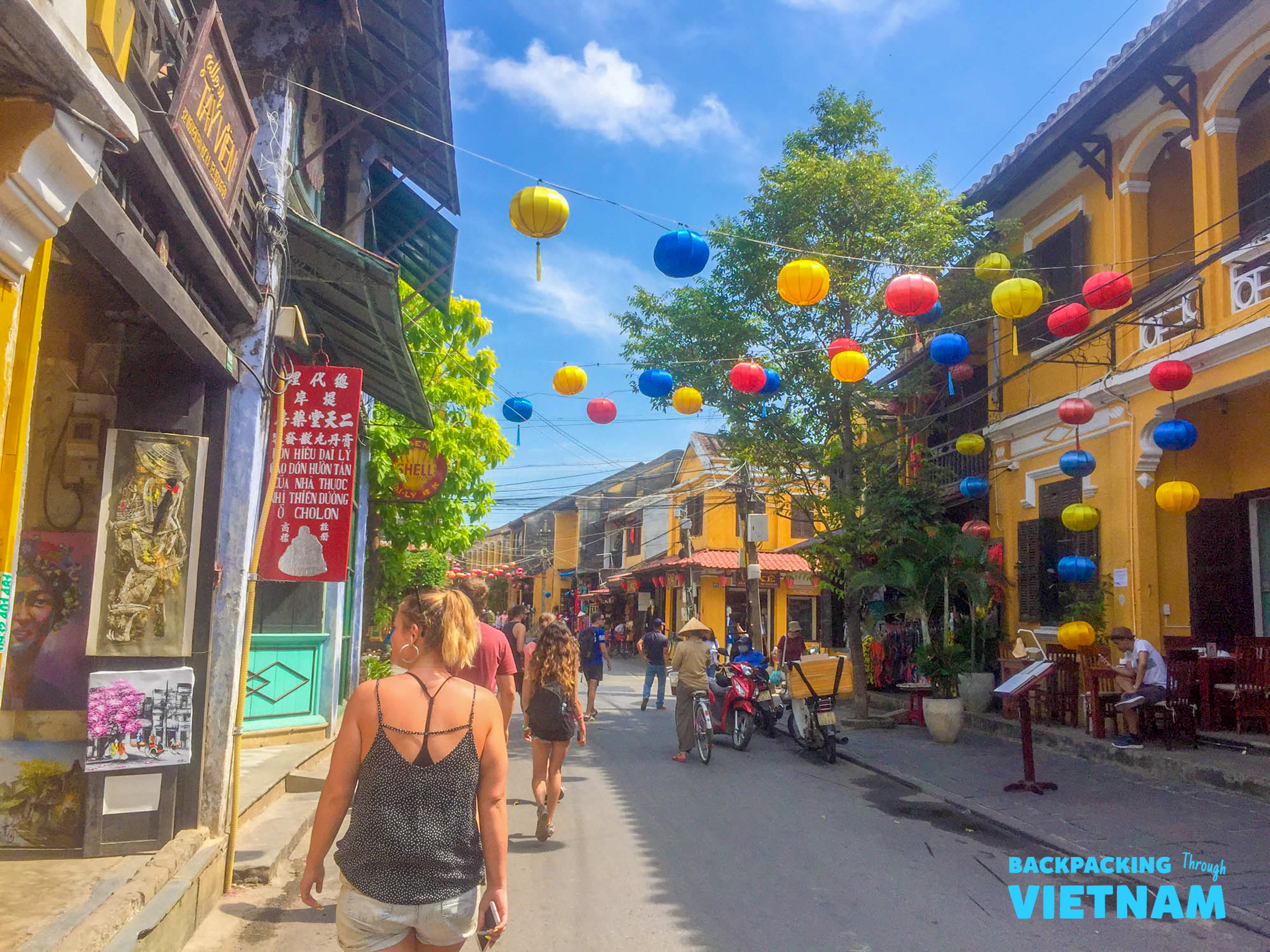 Backpackers explore the charming, lantern-lined streets of Hoi An, Vietnam, on a sunny day.