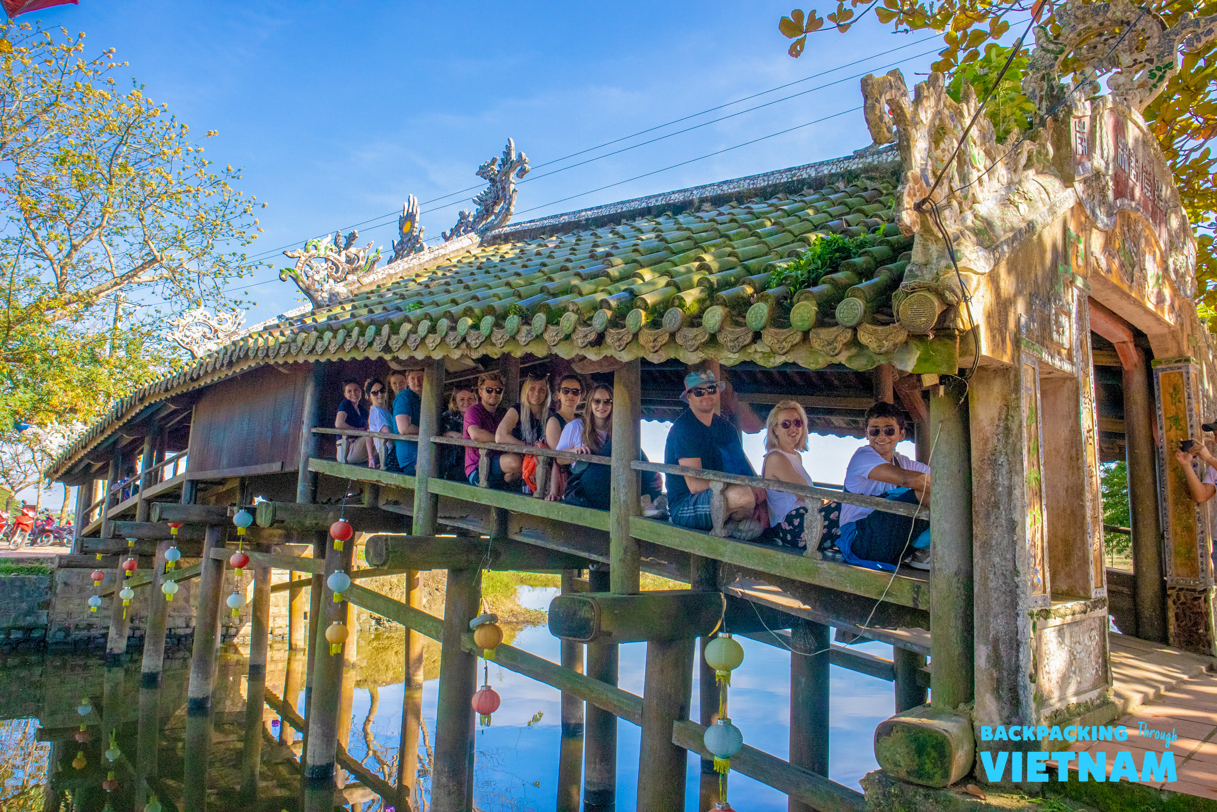 Tourists relax on the historic Japanese Covered Bridge in Hoi An, enjoying the sunny day.