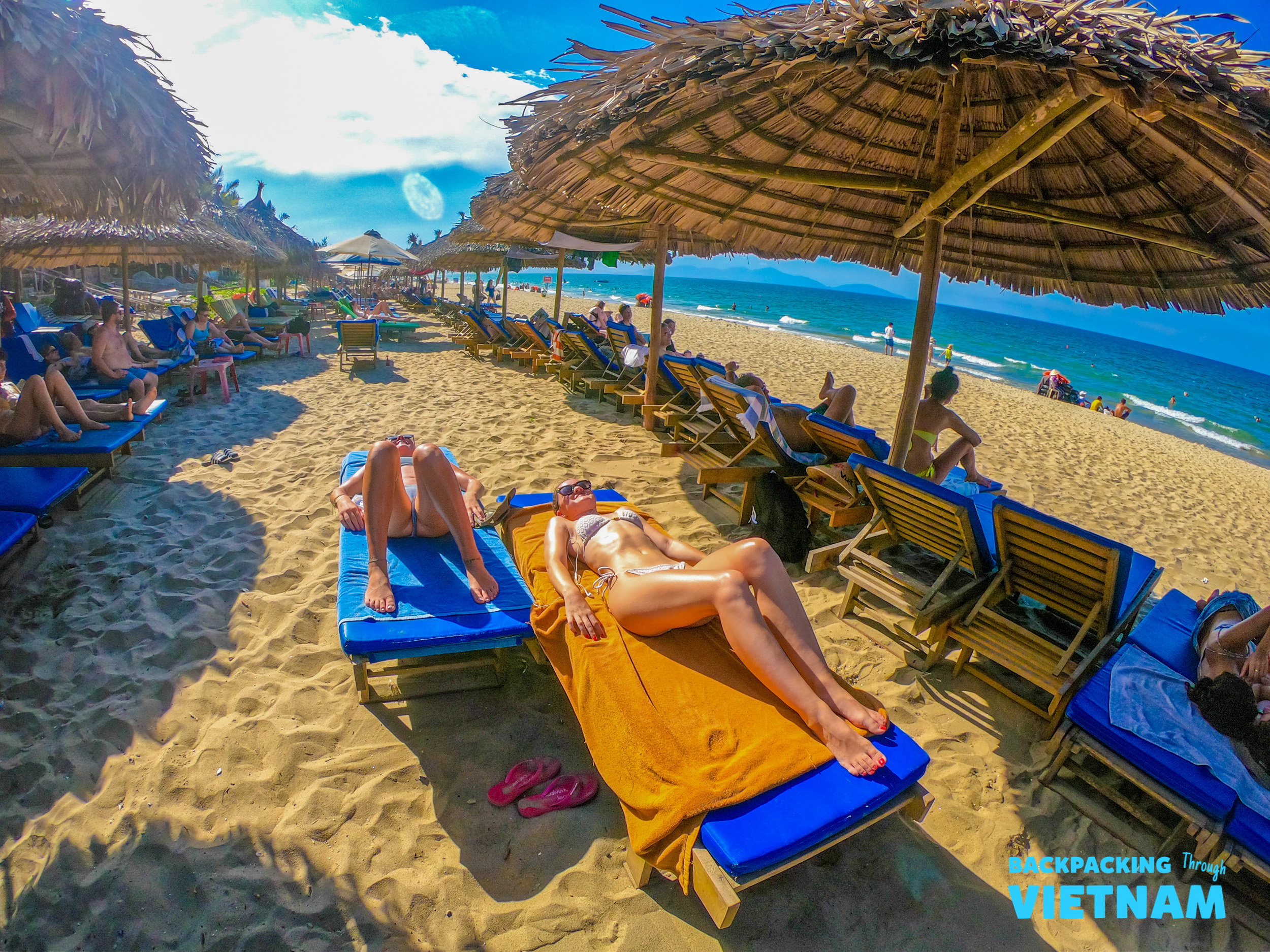 People relaxing on sun loungers under straw umbrellas on An Bang Beach in Hoi An.