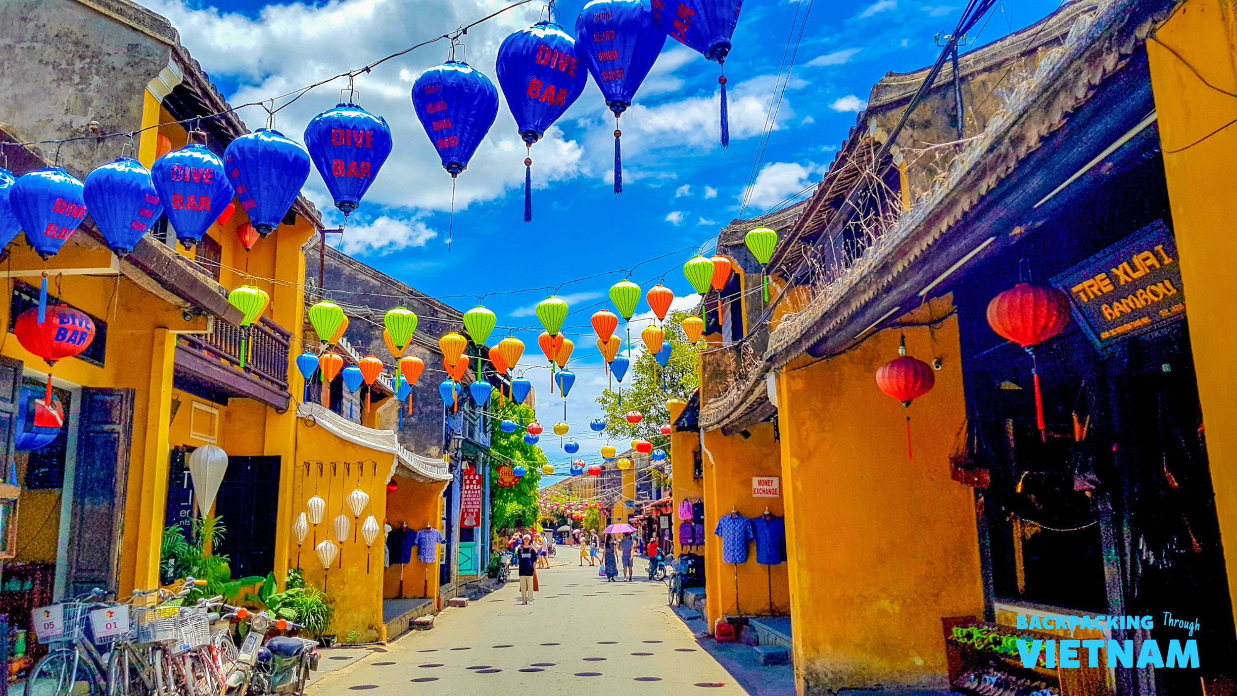 Vibrant Hoi An street adorned with colorful lanterns under a bright blue sky, with people strolling.