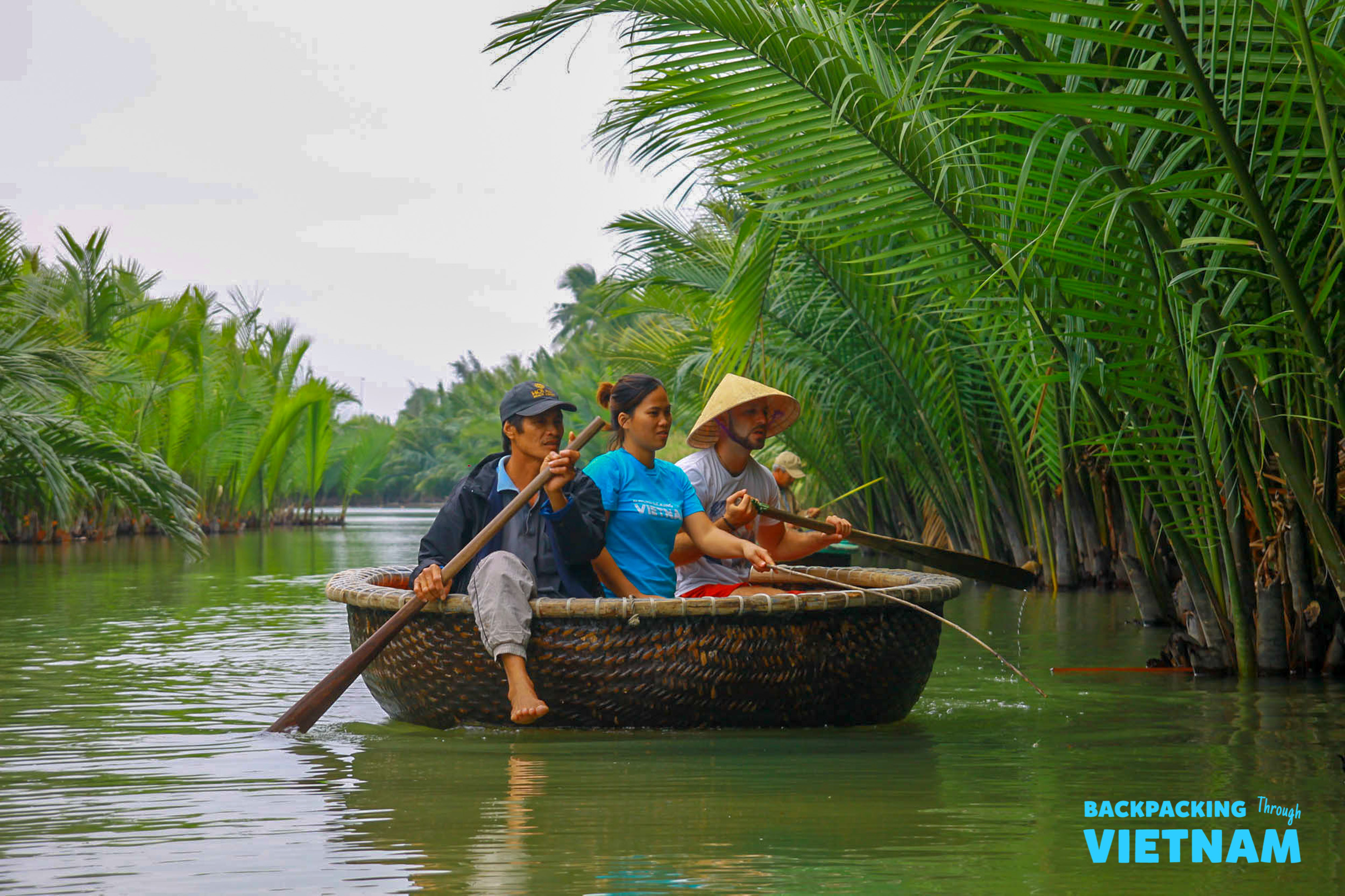 Three people paddle a traditional basket boat through the nipa palm forest in Hoi An.