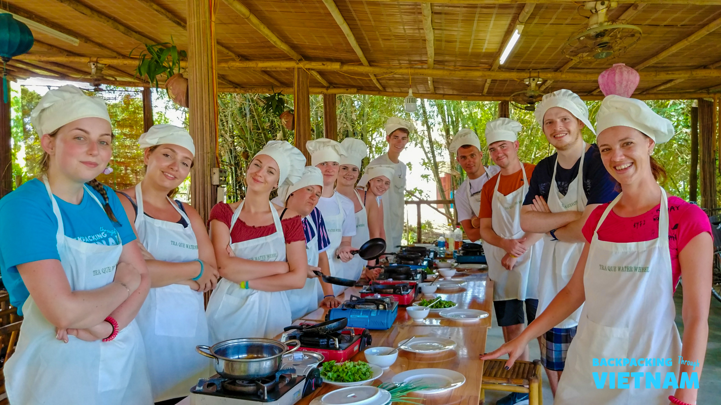 Happy travelers in chef hats and aprons prepare Vietnamese dishes during a cooking class in Hoi An.