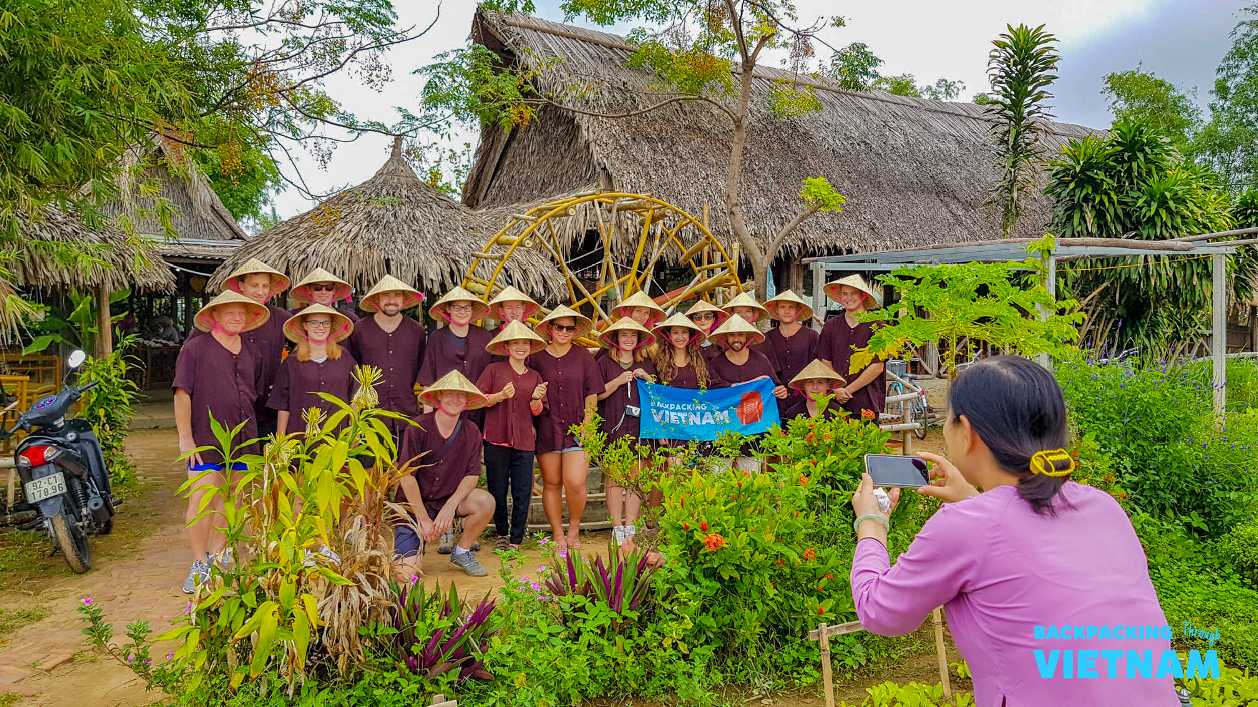 Backpackers in conical hats smile for a photo at a traditional organic farm in Hoi An, Vietnam.