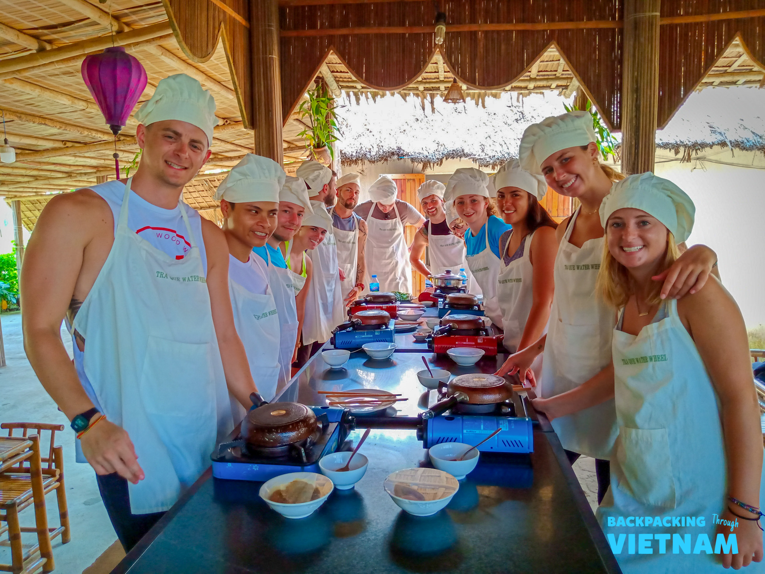 Happy travelers in chef hats learn to cook Vietnamese dishes at an open-air cooking class in Hoi An.