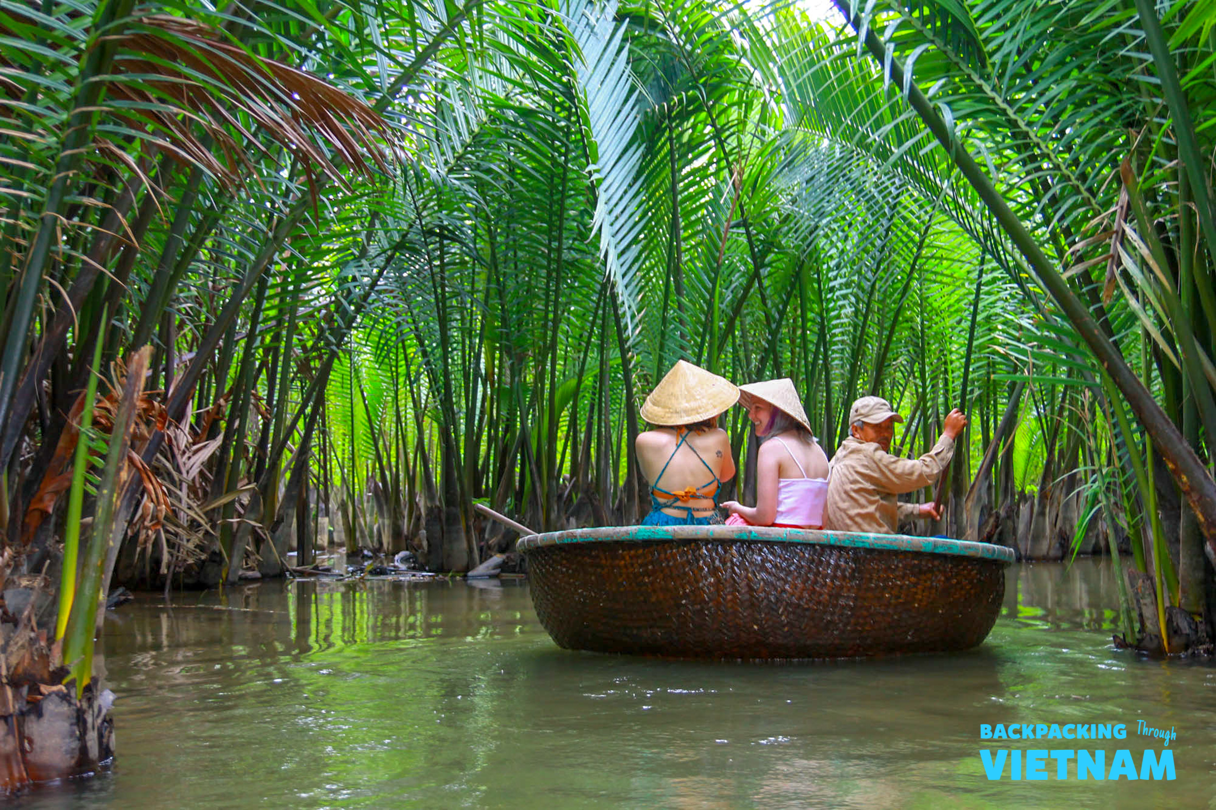 Three travelers in conical hats enjoy a scenic basket boat ride through Hoi An's lush palm forest.