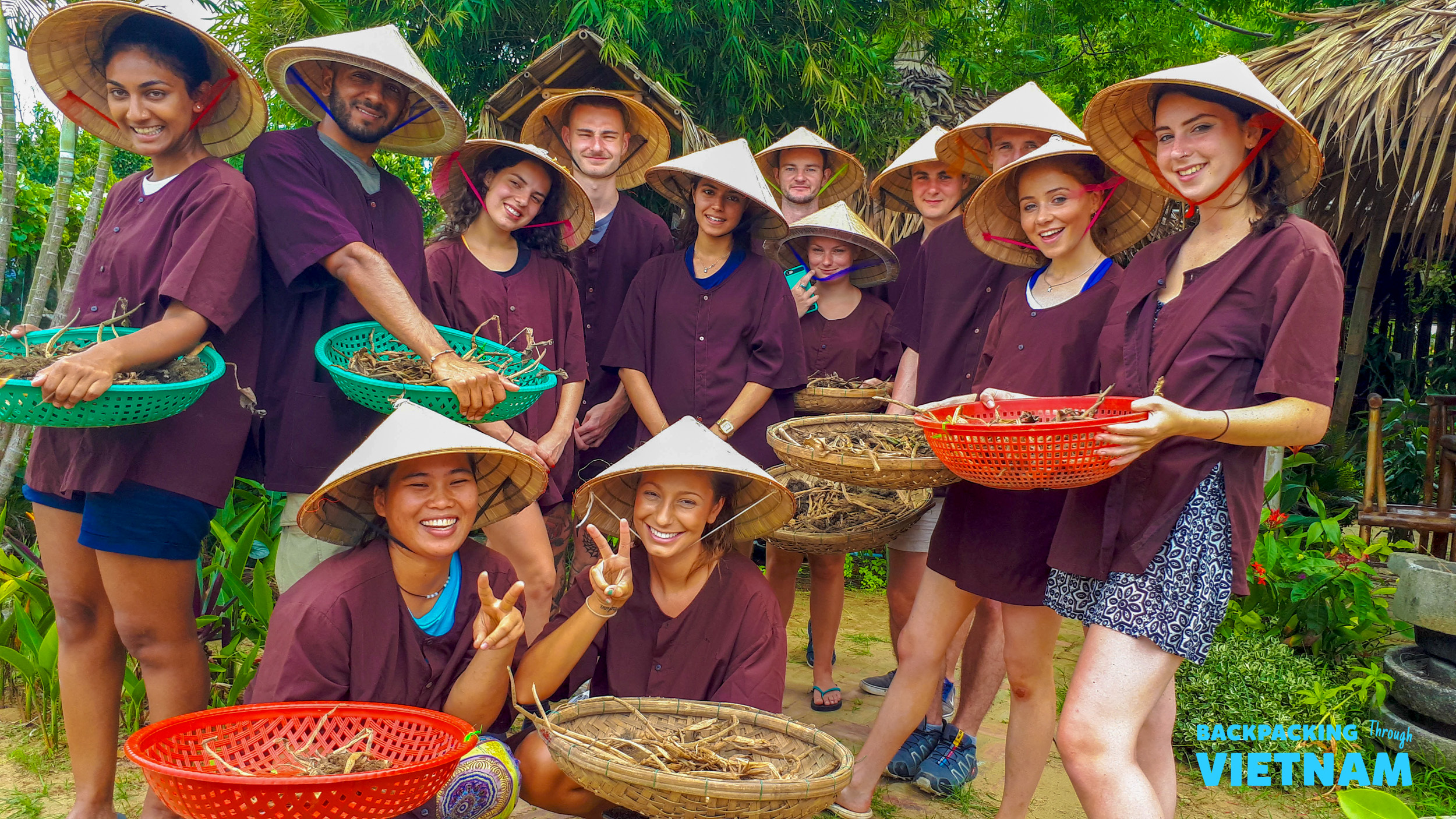 Happy travelers wearing traditional conical hats and holding baskets during a farm visit in Hoi An.