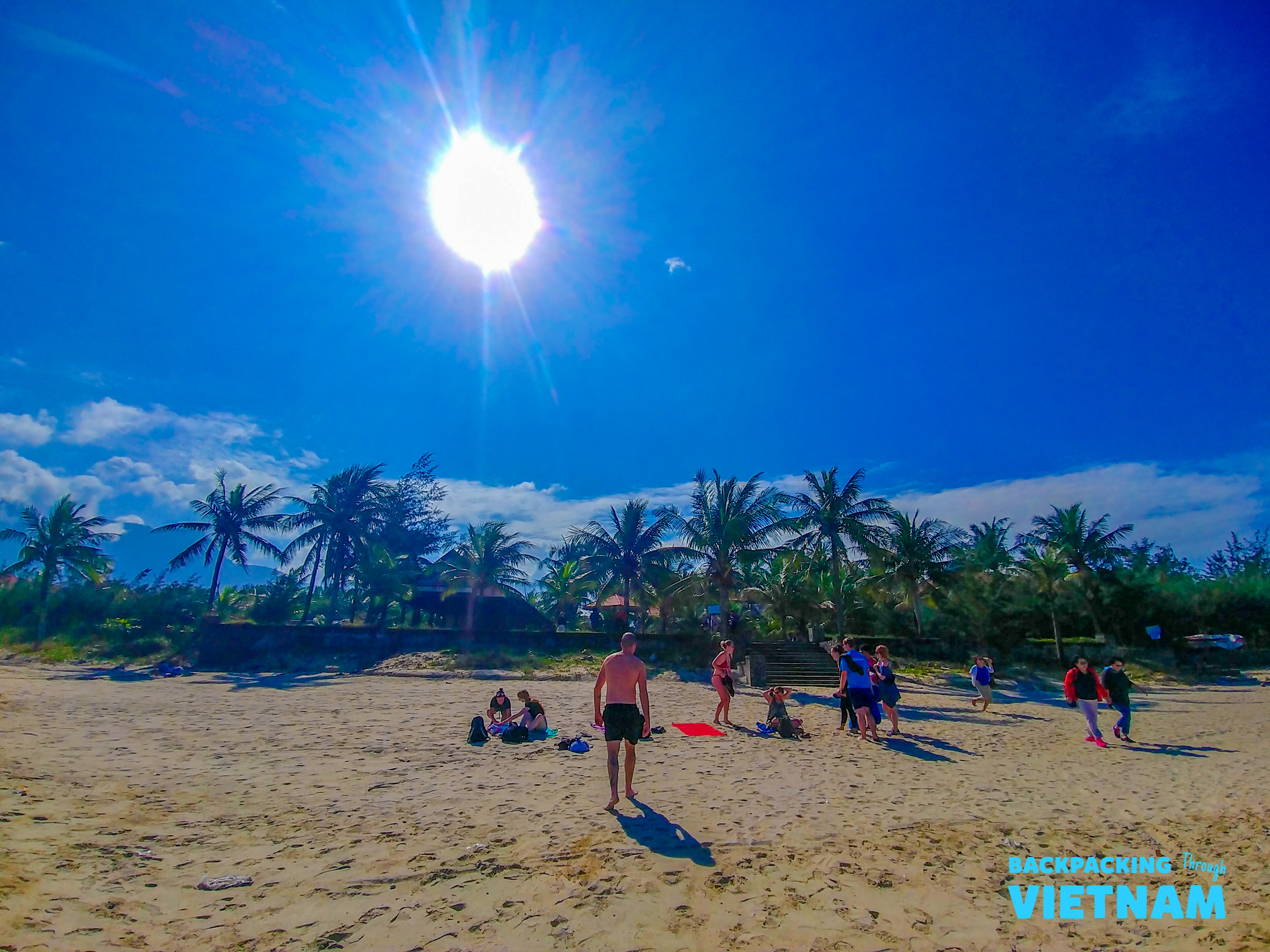 Travelers enjoy a bright, sunny day on the sandy beach of Nha Trang, surrounded by palm trees.